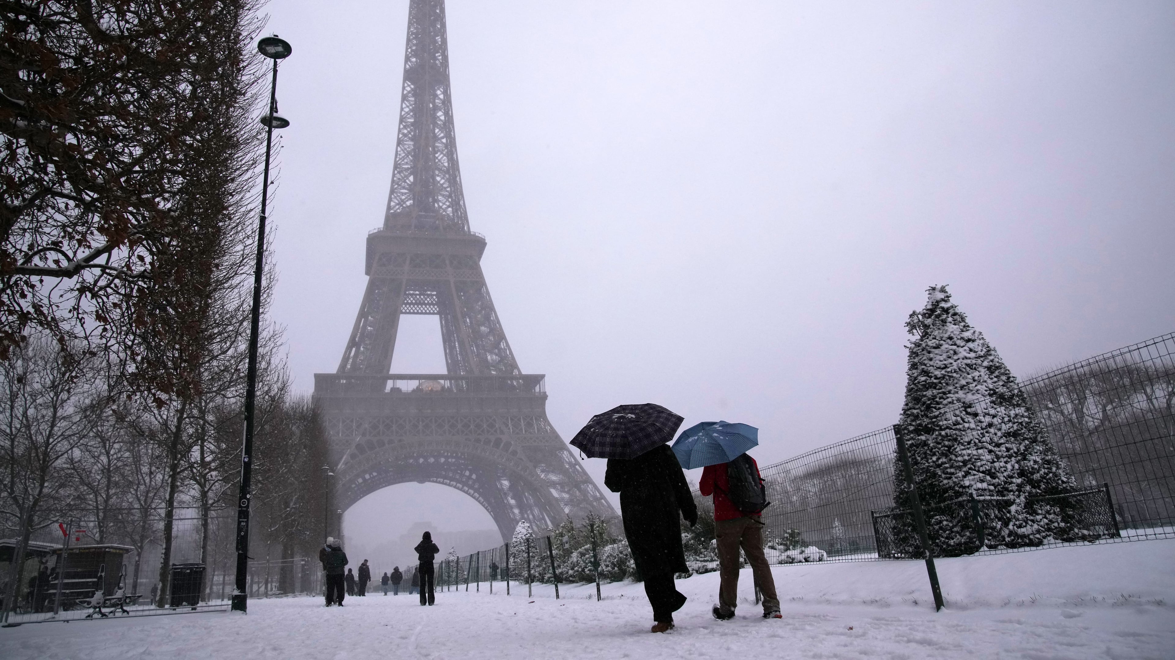 People walk near the Eiffel Tower during a snowfall Wednesday, Jan. 7, 2026 in Paris. (AP Photo/Christophe Ena)
