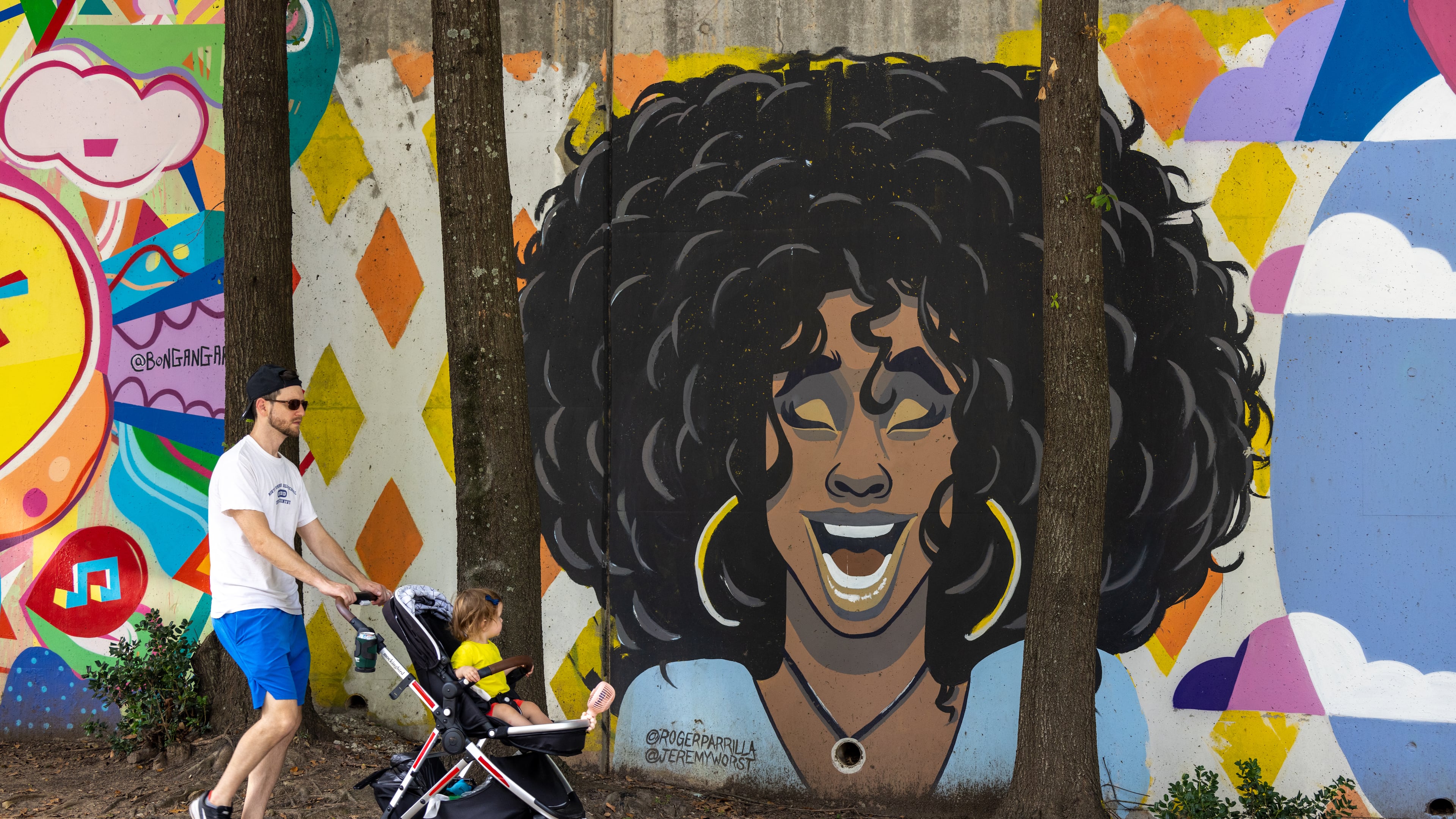 Dad pushing baby stroller in front of Wylie Street murals in Cabbagetown on August 14, 2022