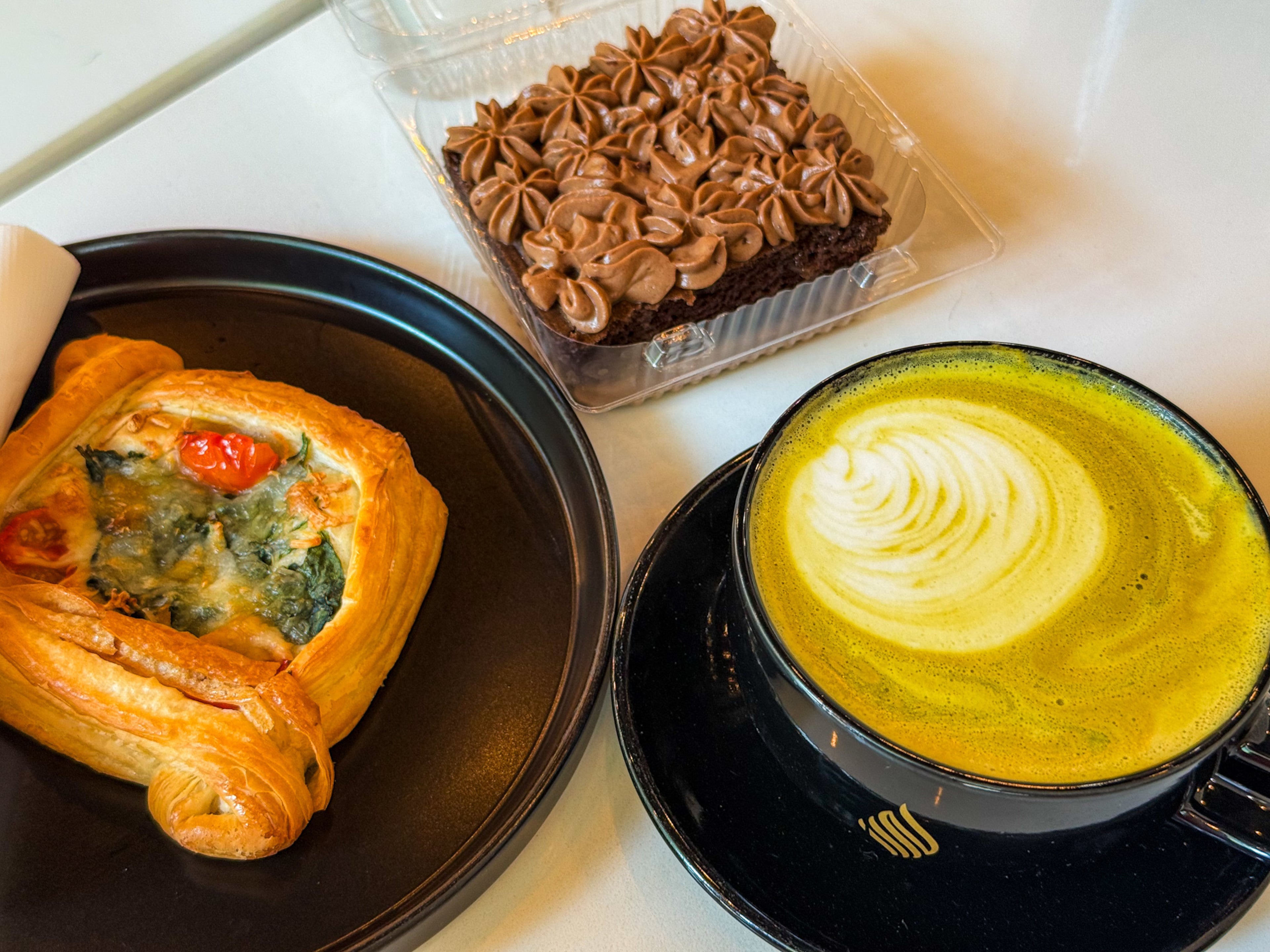 A trio of treats: spinach and tomato cheese Danish, Nutella milk cake and a pistachio latte from Haraz Coffee House. (Henri Hollis/AJC)