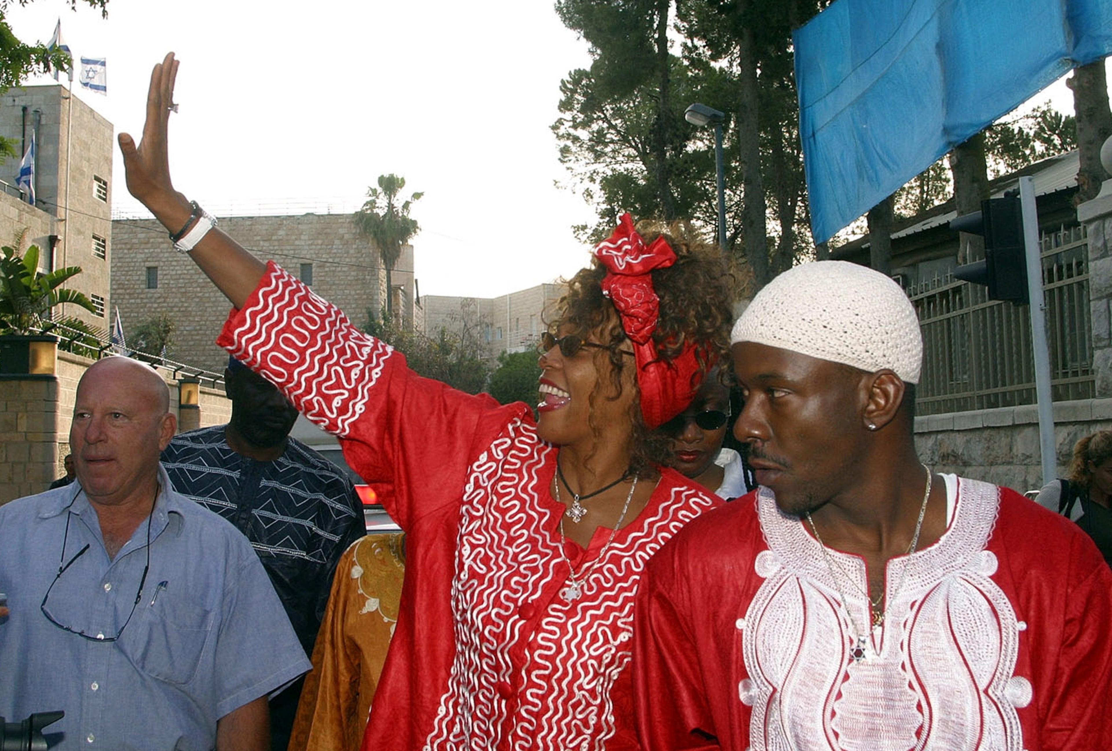 American pop star Whitney Houston waves as she walks down the street with her husband Bobby Brown after a meeting with Israeli Prime Minister Ariel Sharon at the Prime Minister's residence in Jerusalem, Tuesday, May 27, 2003. (AP Photo/Brian Hendler)
