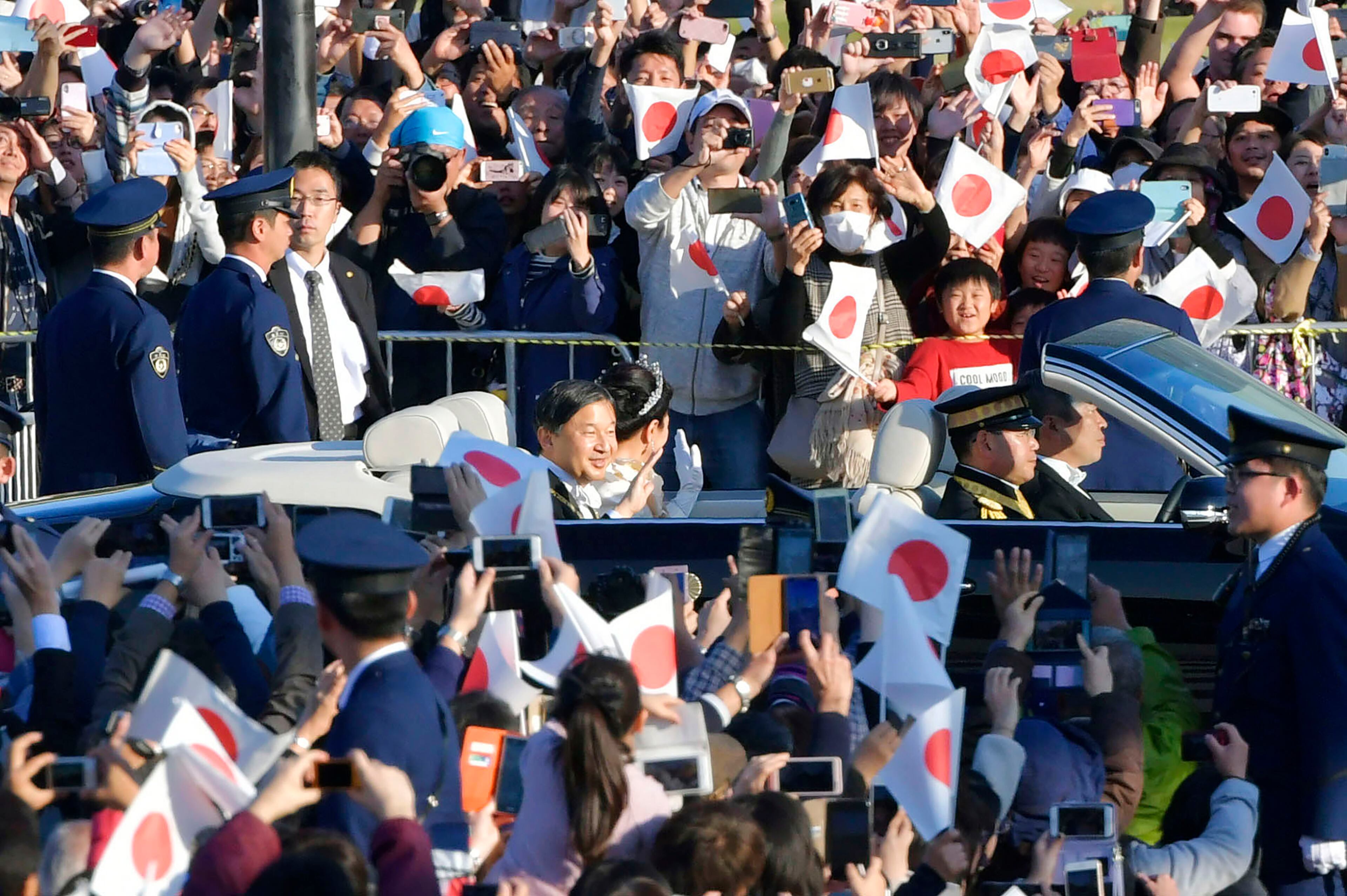 Japanese Emperor Naruhito, center left, and Empress Masako, center right, wave during the royal motorcade in Tokyo, Sunday, Nov. 10, 2019. Naruhito and Masako waved and smiled from an open car in a motorcade marking his enthronement Sunday before hundreds of thousands of delighted well-wishers who cheered, waved small flags and took photos from both sides of packed sidewalks. (Kyodo News via AP)