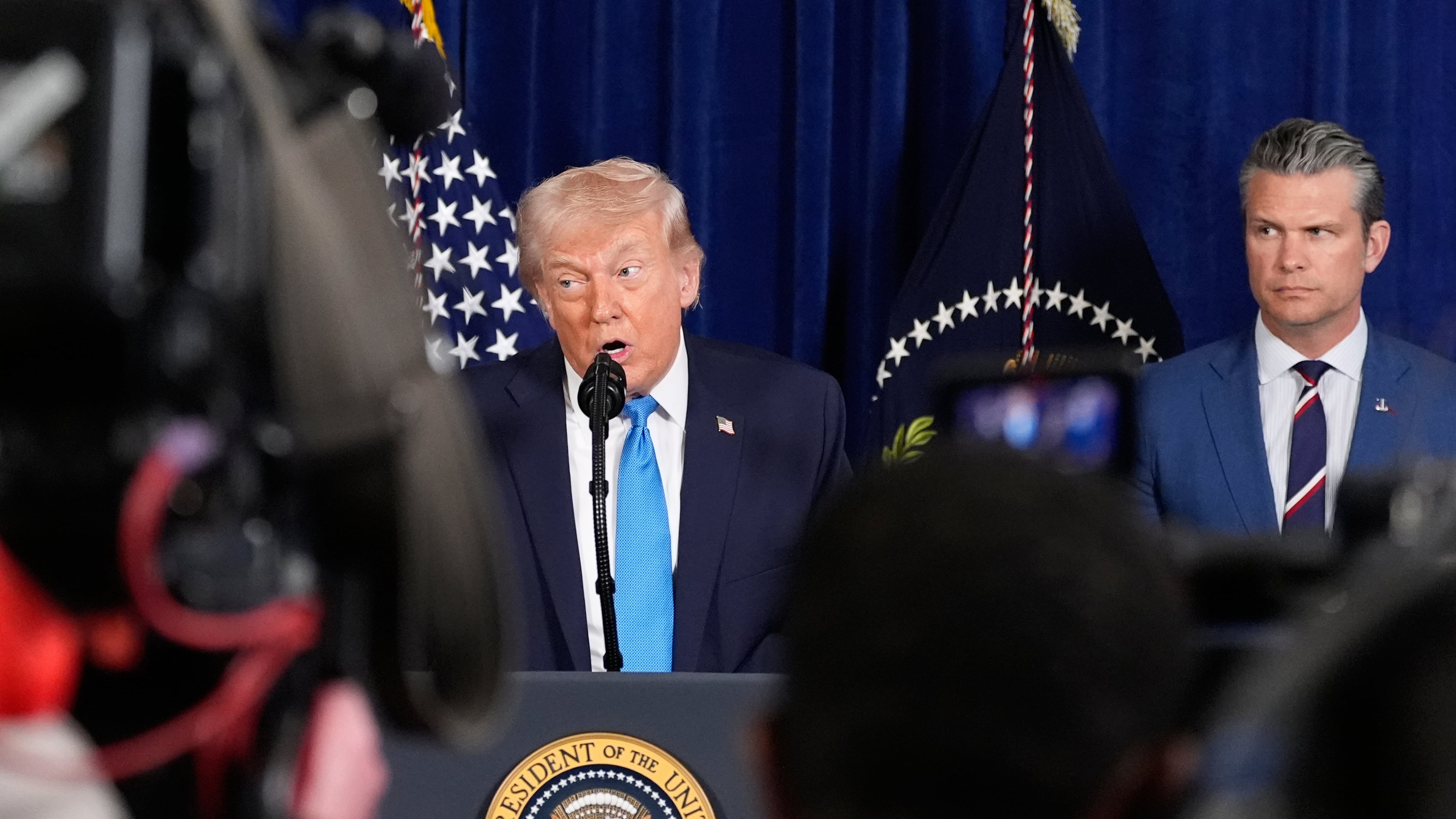 President Donald Trump speaks at his Mar-a-Lago club, Saturday, Jan. 3, 2026, in Palm Beach, Fla., as Defense Secretary Pete Hegseth listens. (AP Photo/Alex Brandon)