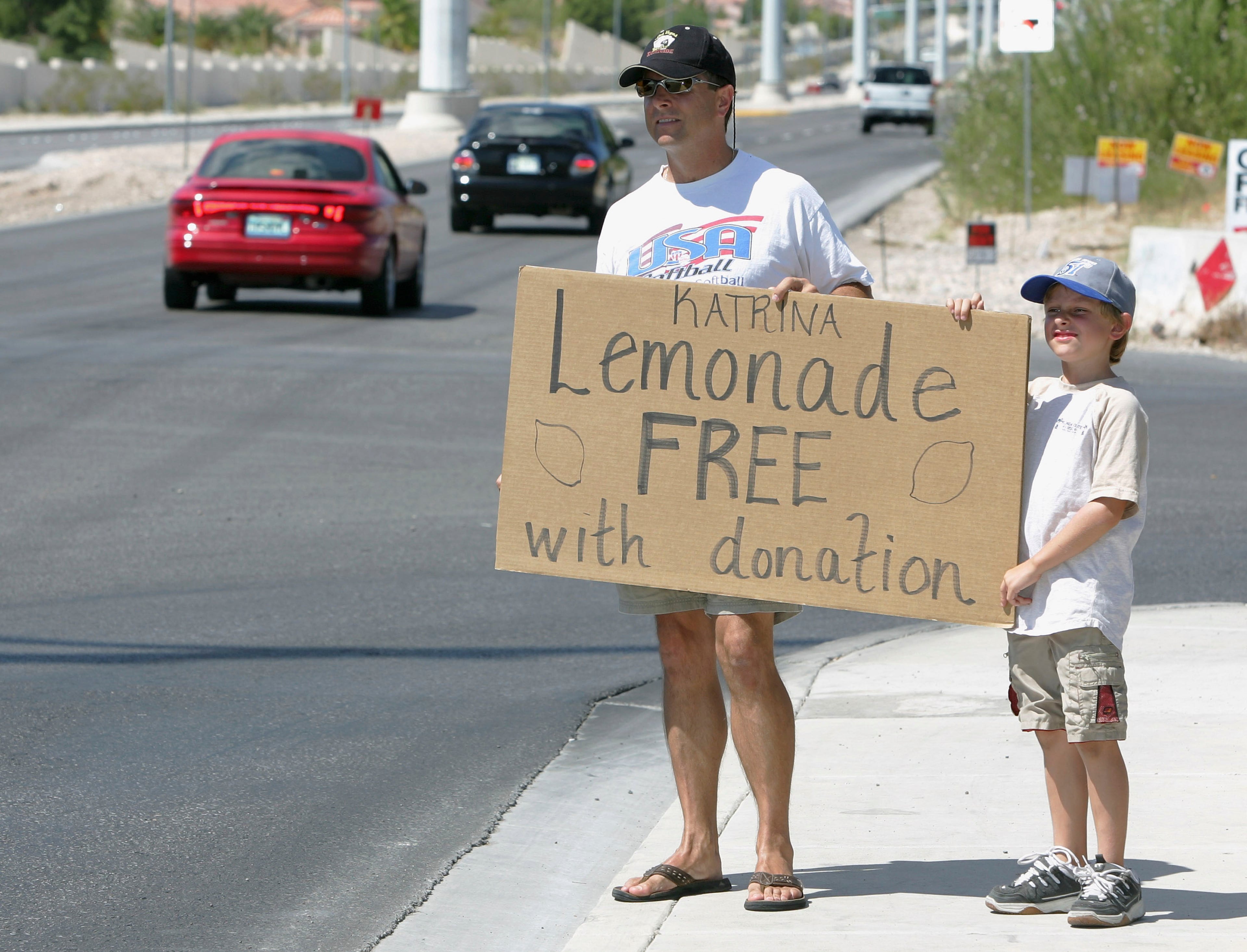 Las Vegas Metropolitan Police Det. Dean O'Kelley and his son Noah O'Kelley, 8, hold a sign alerting motorists of their offer of lemonade in exchange for donations for Hurricane Katrina relief outside a 7-Eleven convenience store September 3, 2005 in Las Vegas, Nevada. The O'Kelley family has been taking donations for victims of Katrina for two days. They plan to give the money, as well as the money from a weekend vacation they canceled, to the Samaritan's Purse International Relief fund. (Photo by Ethan Miller/Getty Images)
