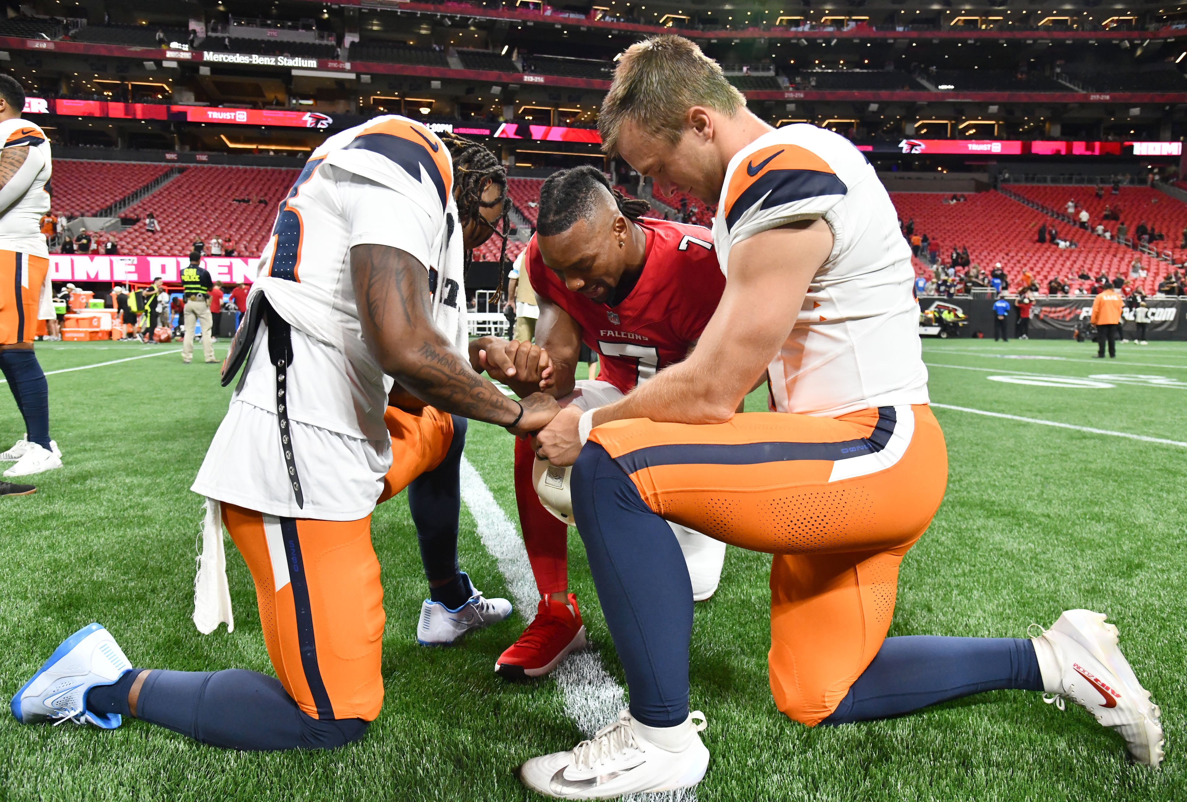 Falcons running back Bijan Robinson (center) holds hands with Broncos cornerback Jahdae Barron (left) and Broncos quarterback Sam Ehlinger as they pray after their preseason game at Mercedes-Benz Stadium on Friday, Aug. 14, 2026, in Atlanta. (Hyosub Shin/AJC)