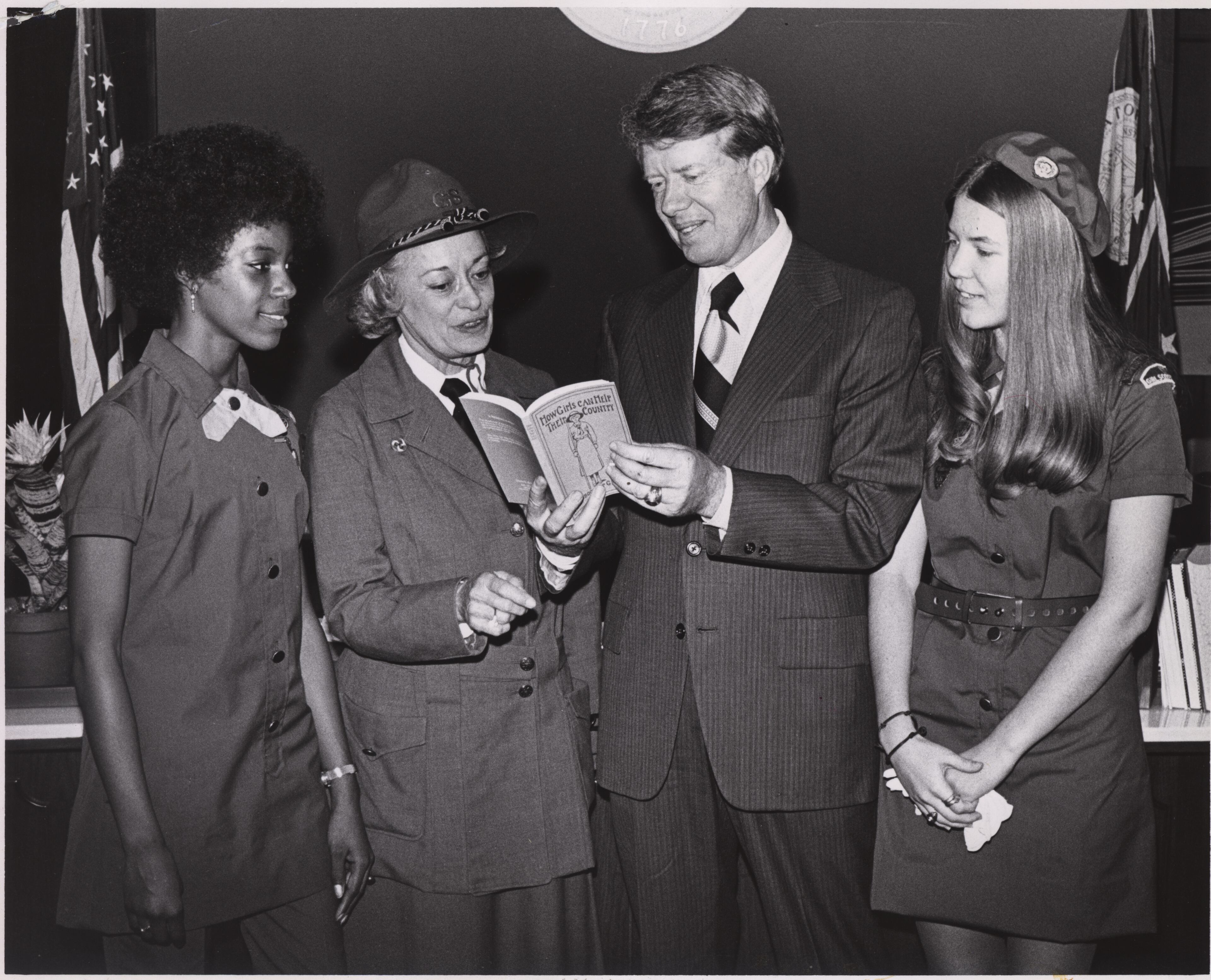 The Girl Scouts celebrate their 60th birthday with then-Georgia Gov. Jimmy Carter in 1972. Mrs. L. Powell Gahagan, president of the Girl Scout Council of Savannah, Georgia, where Girl Scouting started, wears a 1913 Girl Scout uniform. Gahagan has handed the future president a copy of the first Girl Scouting manual, titled "How Girls Can Help Their Country." With Carter and Gahagan are Girl Scouts Myrna Taylor (left) and Amy Stine (right).