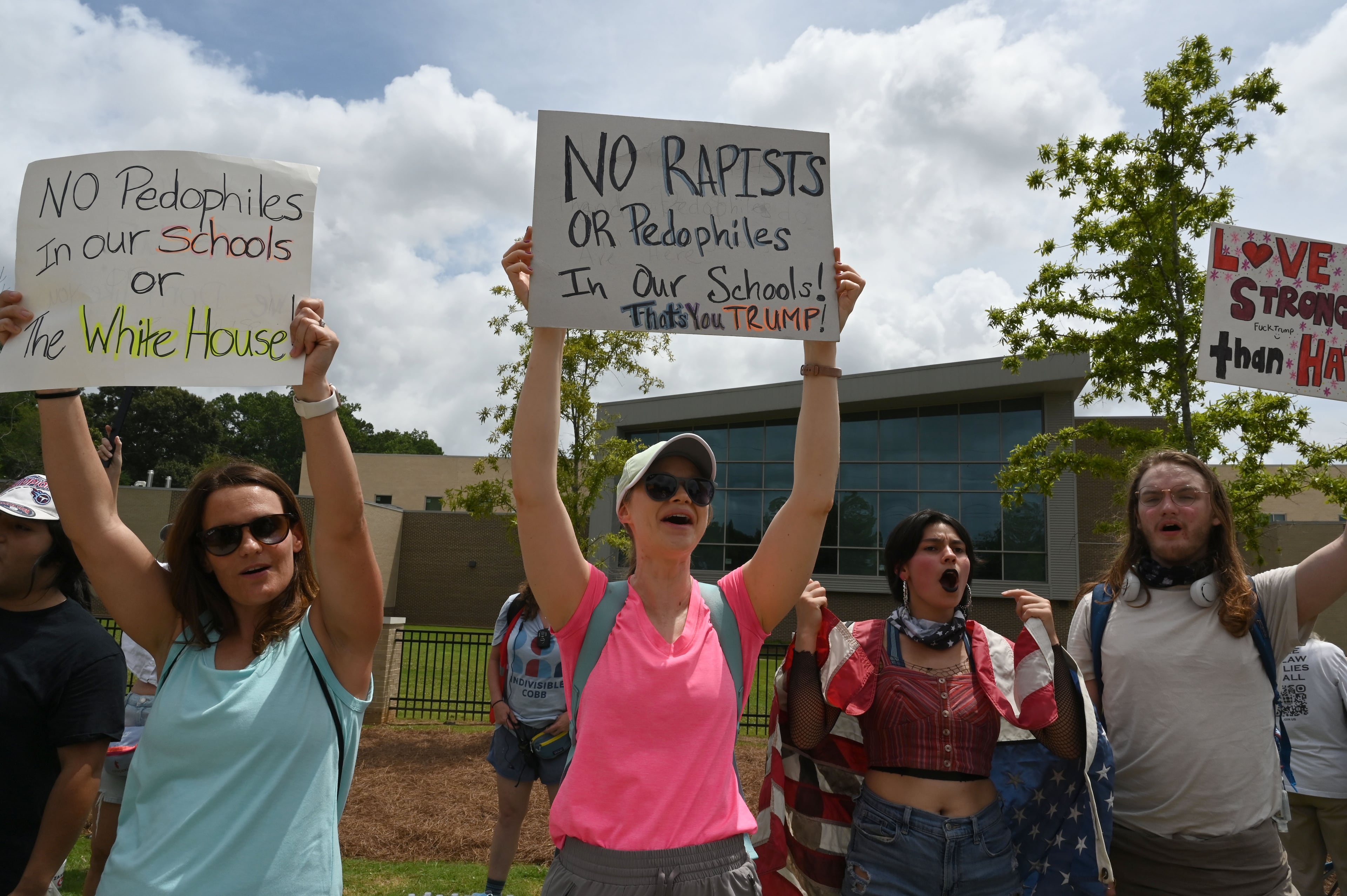 Protesters opposed to President Donald Trump's visit hold signs and line a street as he arrives outside Wheeler High School on Wednesday, July 22, 2026, in Marietta. President Donald Trump is visiting Cobb County’s Wheeler High School on Wednesday to promote a new investment account for children. (Hyosub Shin/AJC)