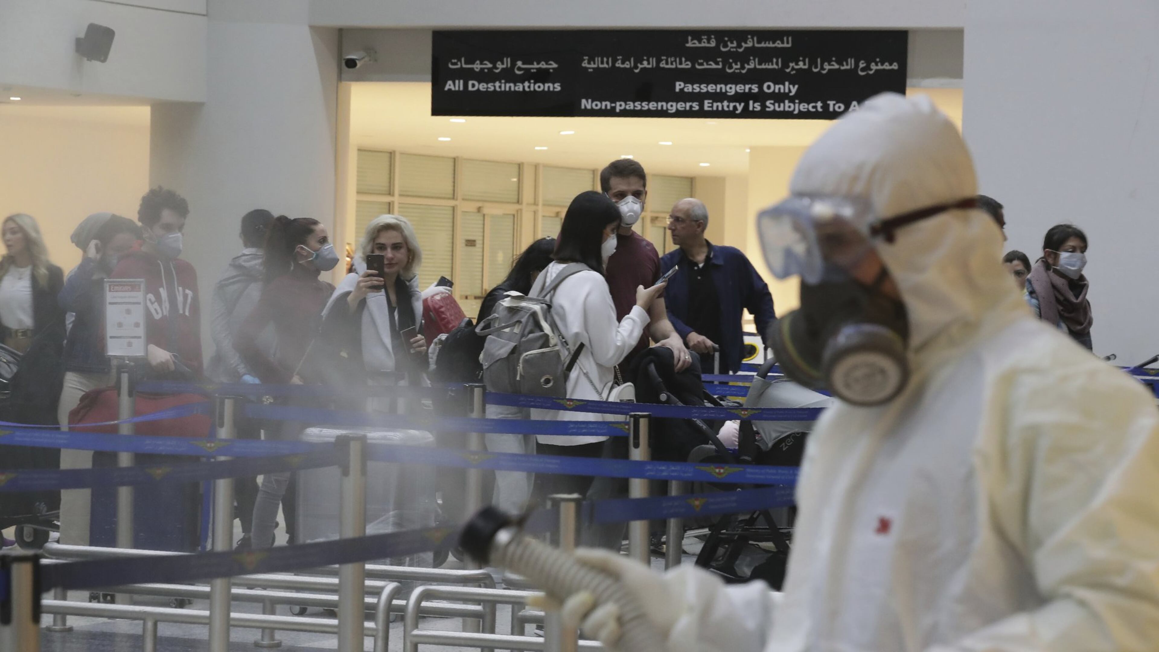 Passengers line up as workers wearing protective gear spray disinfectant as a precaution against the coronavirus outbreak, in the departure terminal at the Rafik Hariri International Airport, in Beirut, Lebanon, Thursday, March 5, 2020. The novel coronavirus has infected more than 80,000 people globally, causing around 2,700 deaths, mainly in China. (AP Photo/Hassan Ammar)