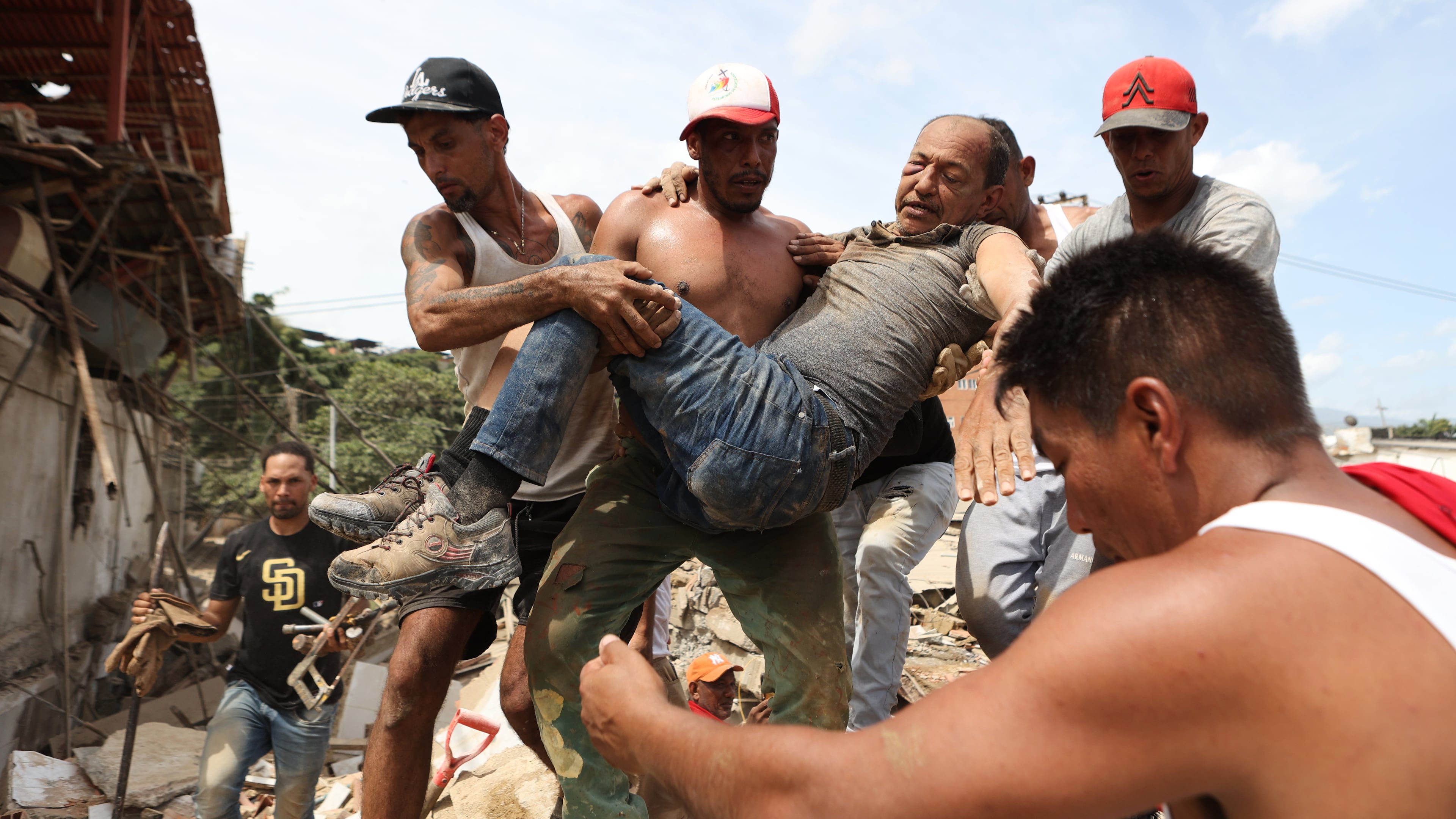 Neighbors carry a man rescued from the rubble of a collapsed building the day after earthquakes struck La Guaira, Venezuela, Thursday, June 25, 2026. (AP Photo/Pedro Mattey)
