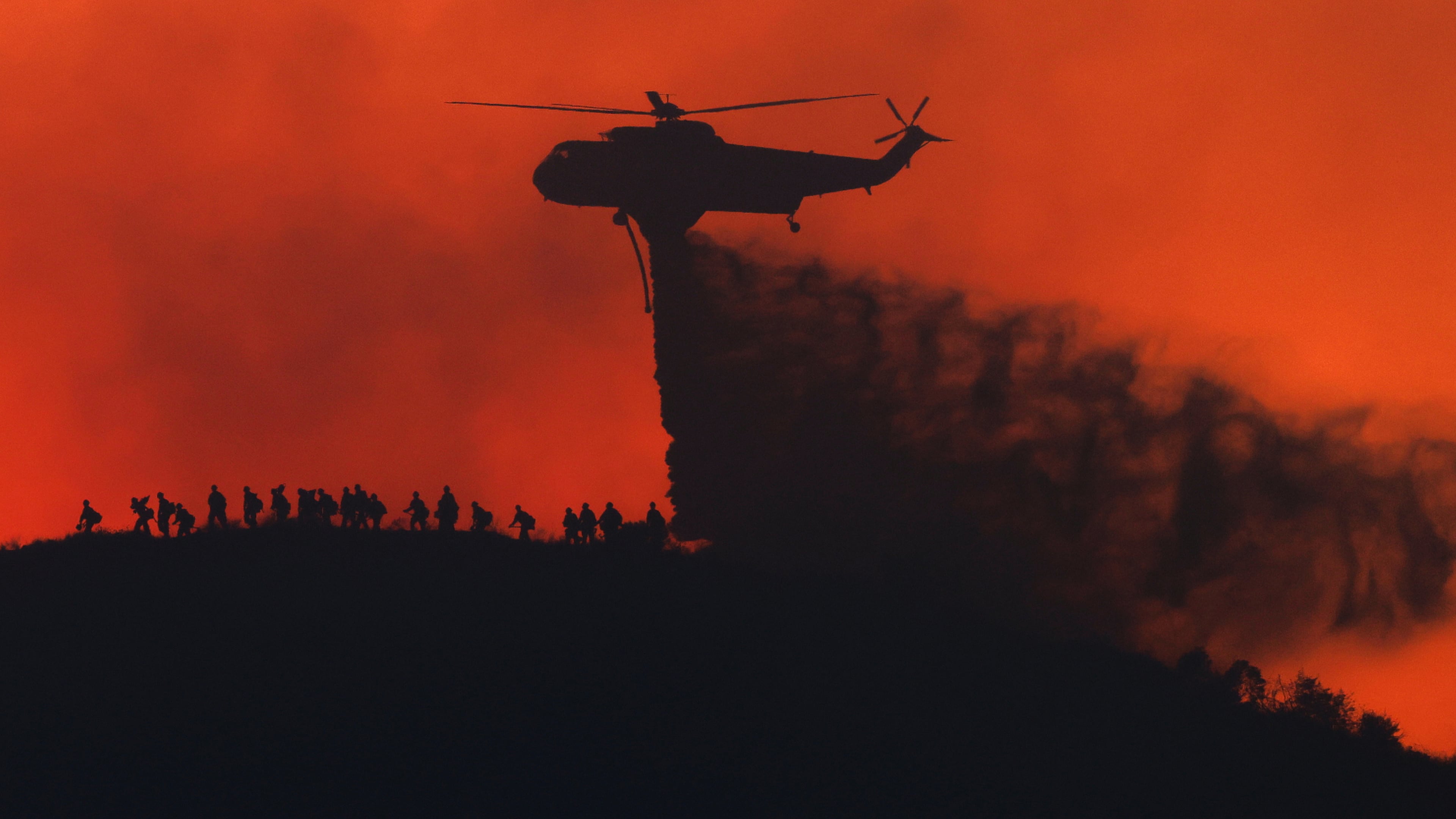 A water tanker drops water while firefighters walk below, as the Sandy Fire approaches, Tuesday, May 19, 2026, in Simi Valley, Calif. (AP Photo/Caroline Brehman)