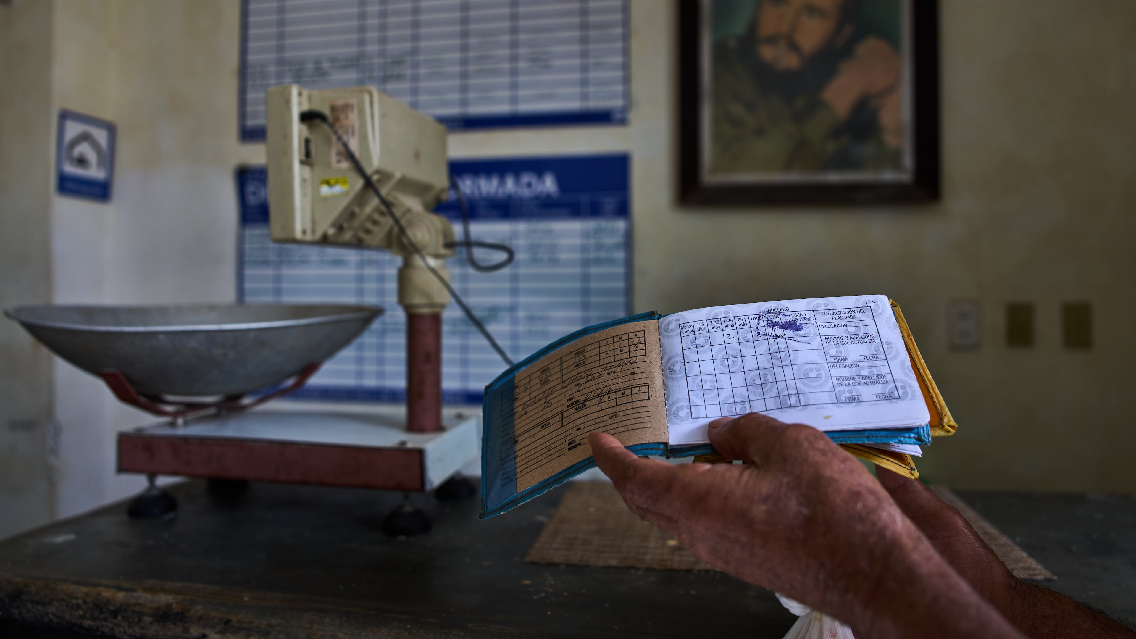 A man shows his ration book known as a "libreta," backdropped by a framed image of Fidel Castro, at a state-run bodega in Havana, Cuba, Saturday, May 2, 2026. (AP Photo/Ramon Espinosa)