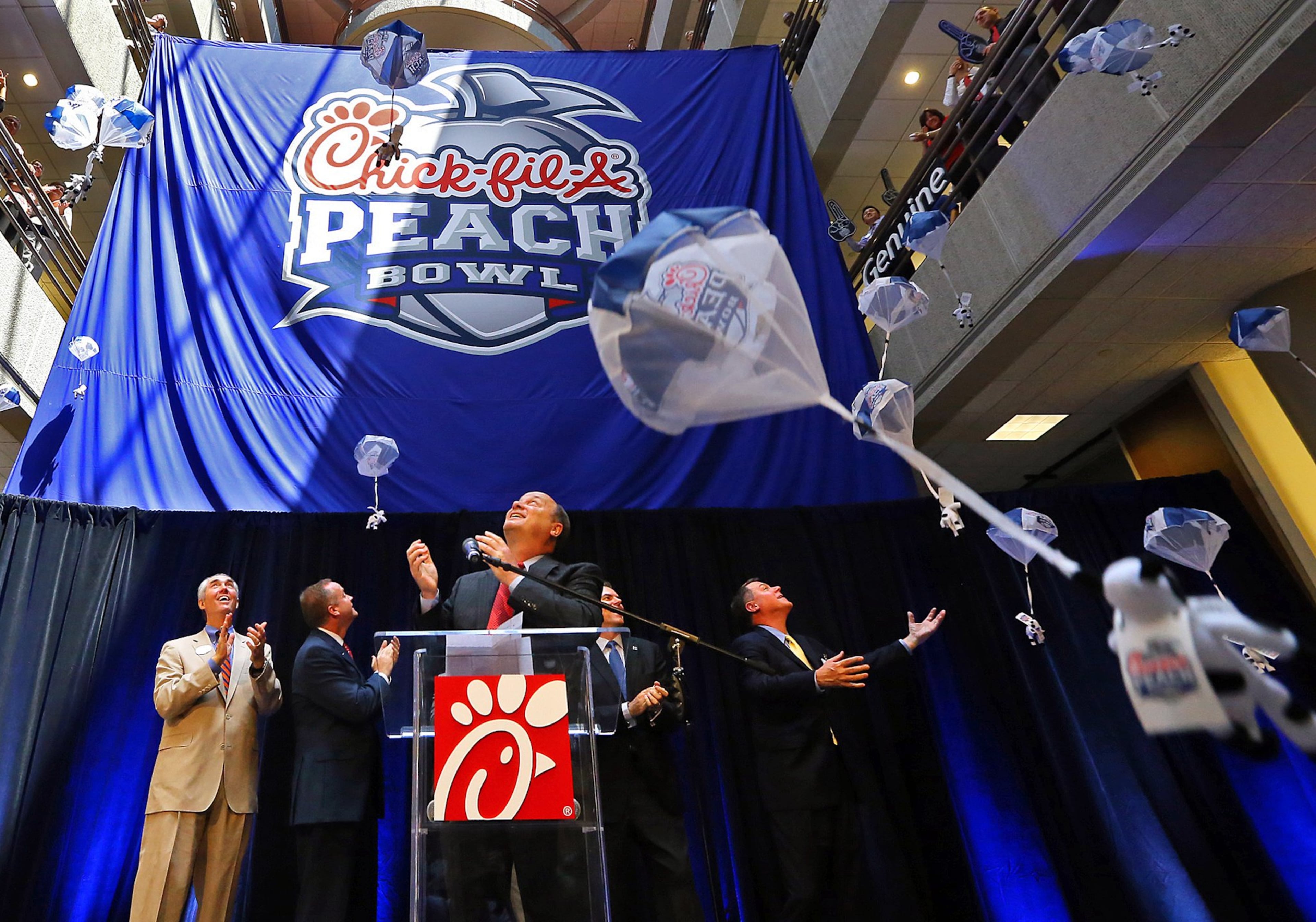 Steve Robinson (from left), Chick-fil-A executive vice president; Michael Kelly, College Football Playoff executive; Gary Stokan, bowl president; Rob Temple, ESPN vice president; and Burke Magnus, ESPN senior vice president, unveil the new Chick-fil-A Peach Bowl logo while parachuting cows drop from the ceiling in 2014. (AJC 2014)