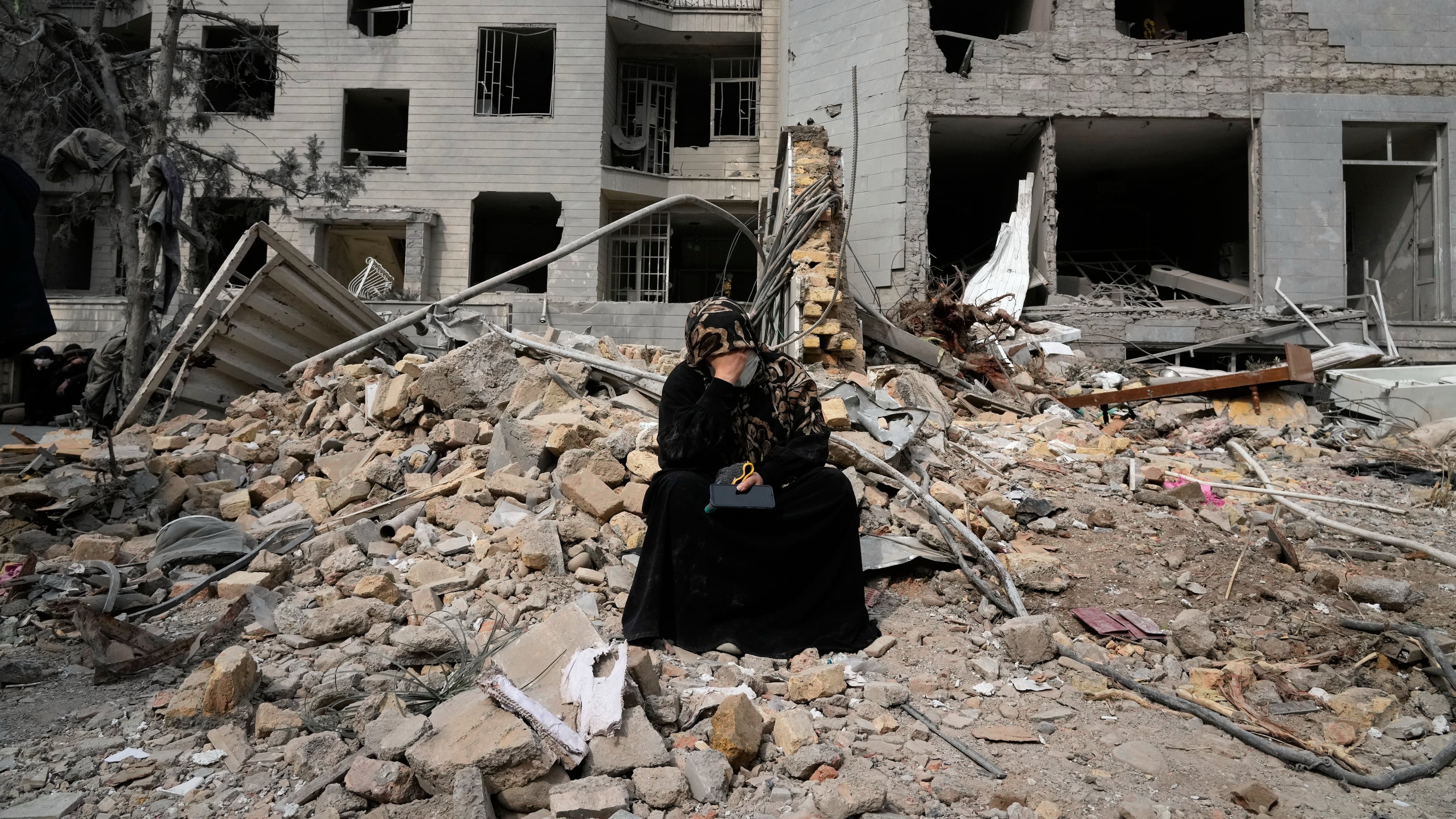 A woman sits on rubble across from a residential building damaged last Monday during the U.S.-Israeli air campaign in Tehran, Iran, Thursday, March 12, 2026. (AP Photo/Vahid Salemi)