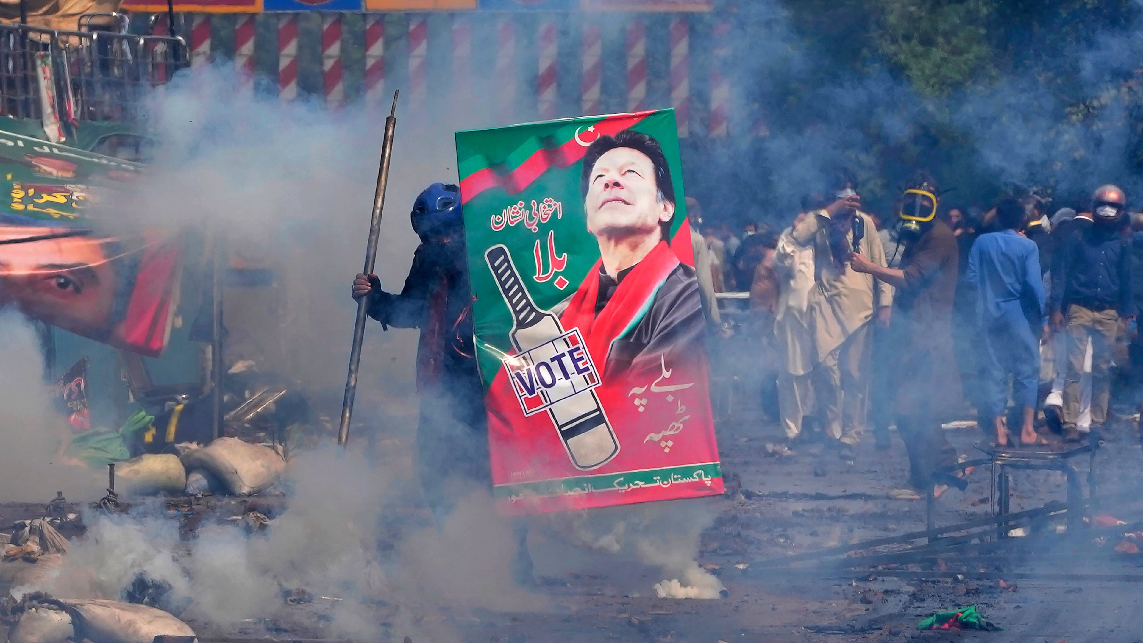 FILE - Supporters of former Prime Minister Imran Khan take cover after riot police officers fire tear gas to disperse them during clashes, in Lahore, Pakistan, Wednesday, March 15, 2023. (AP Photo/K.M. Chaudary, File)