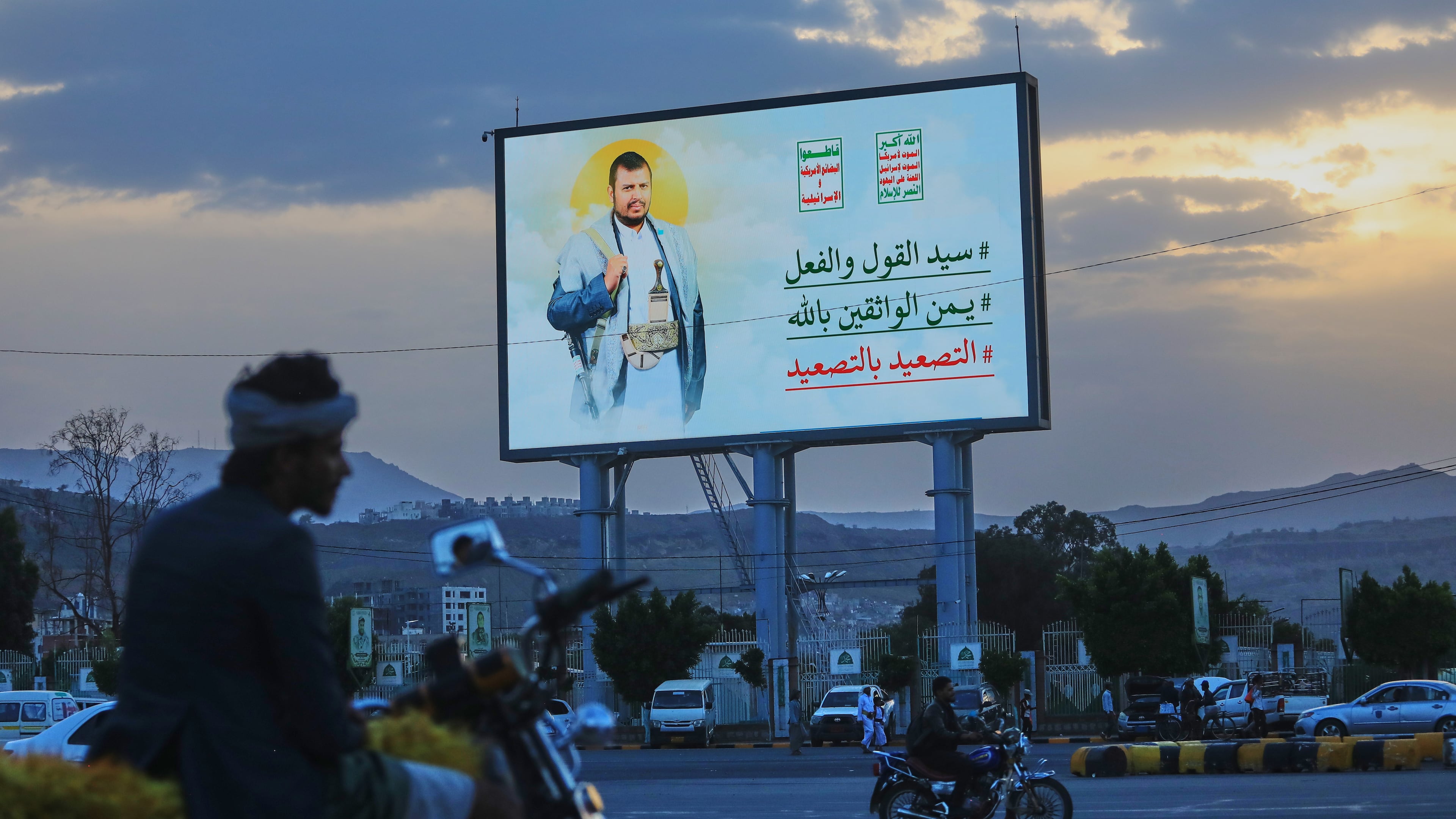 People ride their motorbikes under a billboard showing Houthi leader Abdul Malik al-Houthi with a phrase that reads in Arabic; "master of words and deeds" in Sanaa, Yemen, Monday, Sept. 21, 2026. (AP Photo/Osamah Abdulrahman)