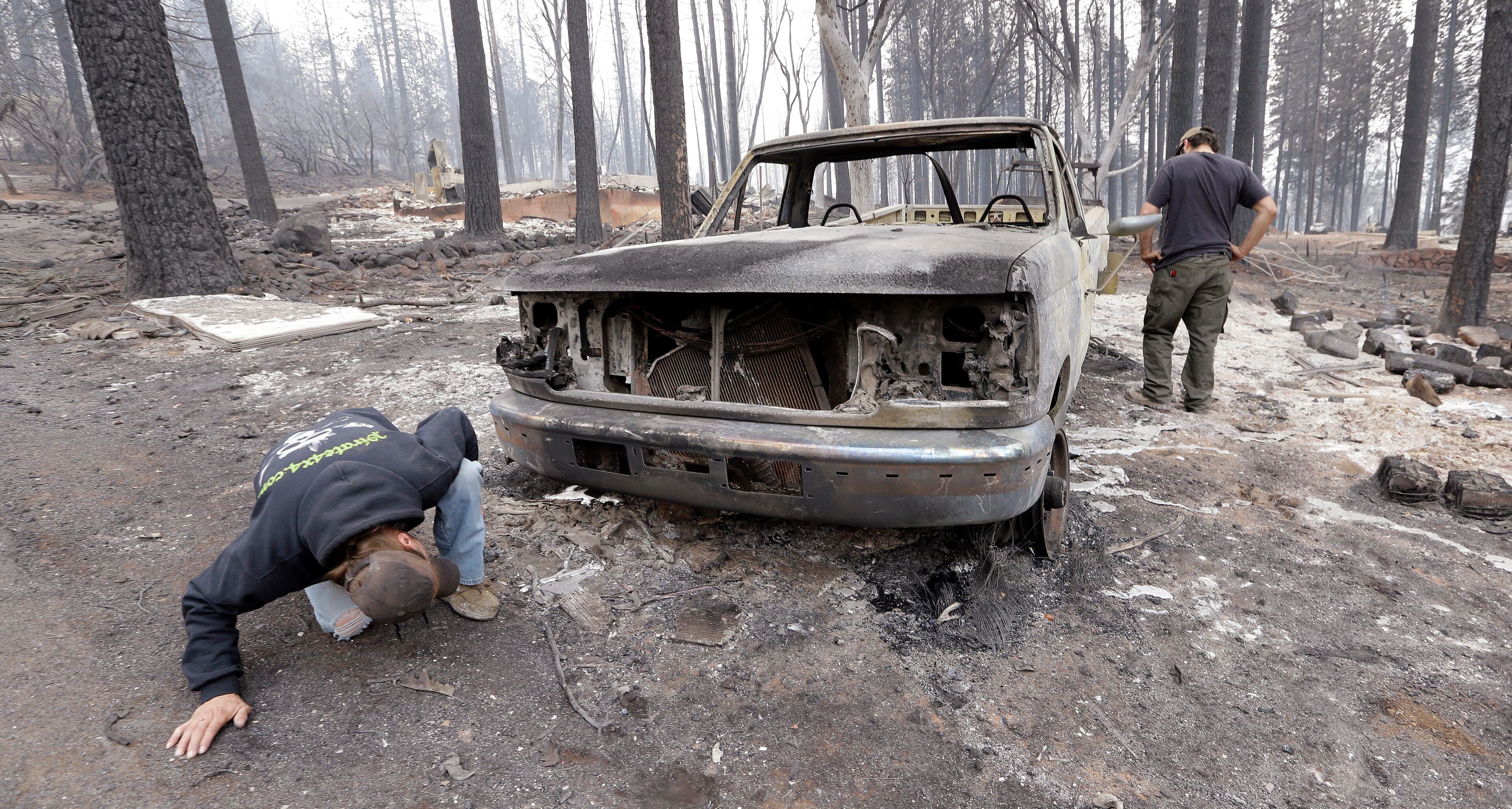 Joel Miller looks under the remains of the pickup truck of his son-in-law Adam Bailey, right, next to the still smoldering remains of Bailey's home Monday, Sept. 14, 2015, in Cobb, Calif. Bailey escaped the flames with his baby Saturday, just before flre roared through the neighborhood of about two dozen homes. Two of California's fastest-burning wildfires in decades overtook several Northern California towns, killing at least one person and destroying hundreds of homes and businesses and sending thousands of residents fleeing highways lined with buildings, guardrails and cars still in flames. (AP Photo/Elaine Thompson)