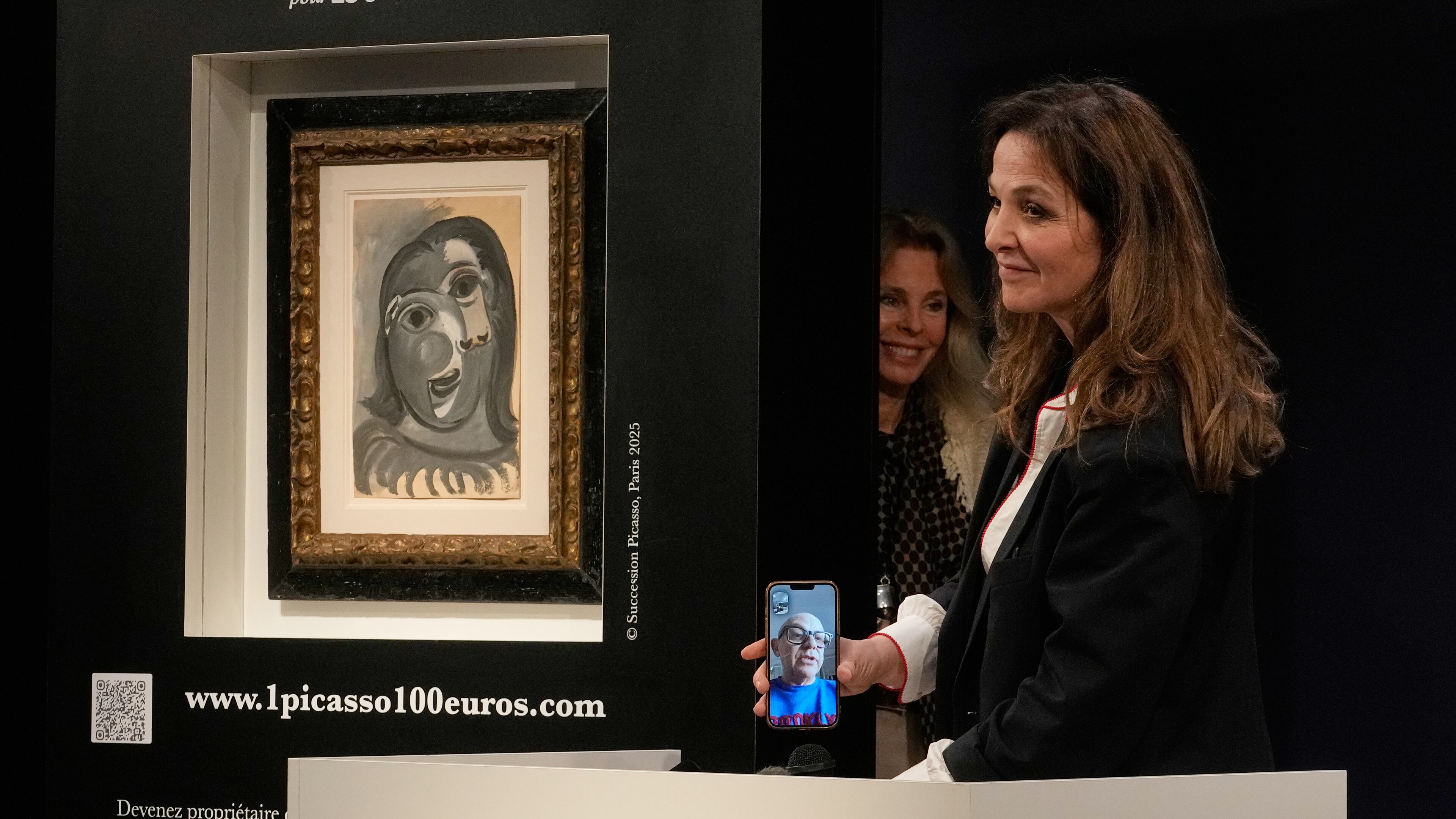 Peri Cochin, right, founder of "1 Picasso for 100 euros," speaks on the phone with the winner, Ari Hodara of Paris, next to the painting 'Head of a Woman' by Pablo Picasso, painted in 1941, after the raffle draw at Christie's in Paris, Tuesday, April 14, 2026, in support of Alzheimer's research. (AP Photo/Michel Euler)