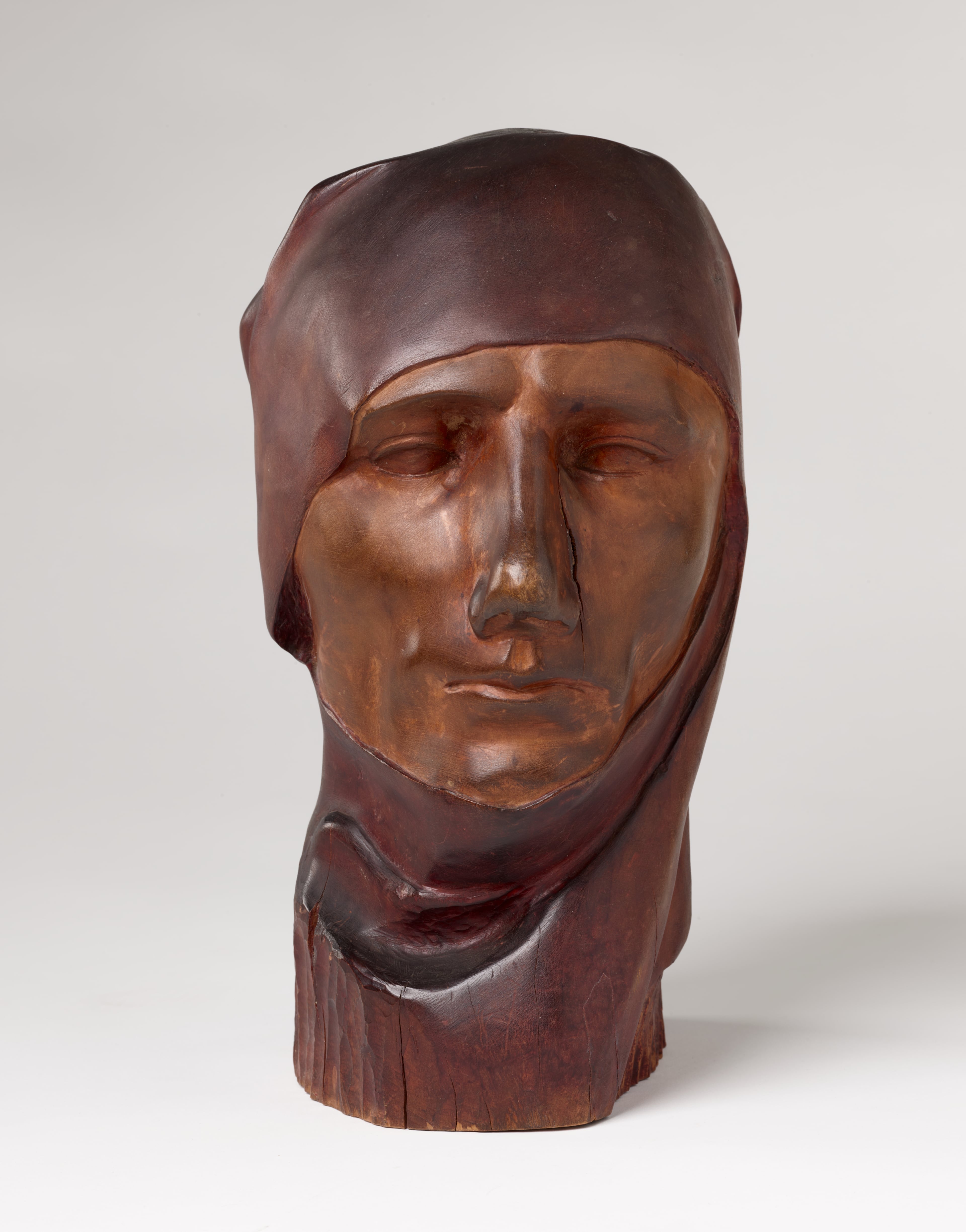 "Discontent" (1929) by Nancy Elizabeth Prophet. Front view of a carved wooden sculpture depicting a serene face wearing a cloth draped around its head. The bust features smooth contours and a crack alongside its nose. (Ccourtesy of Julie Yarborough for Spelman College Museum of Fine Art)