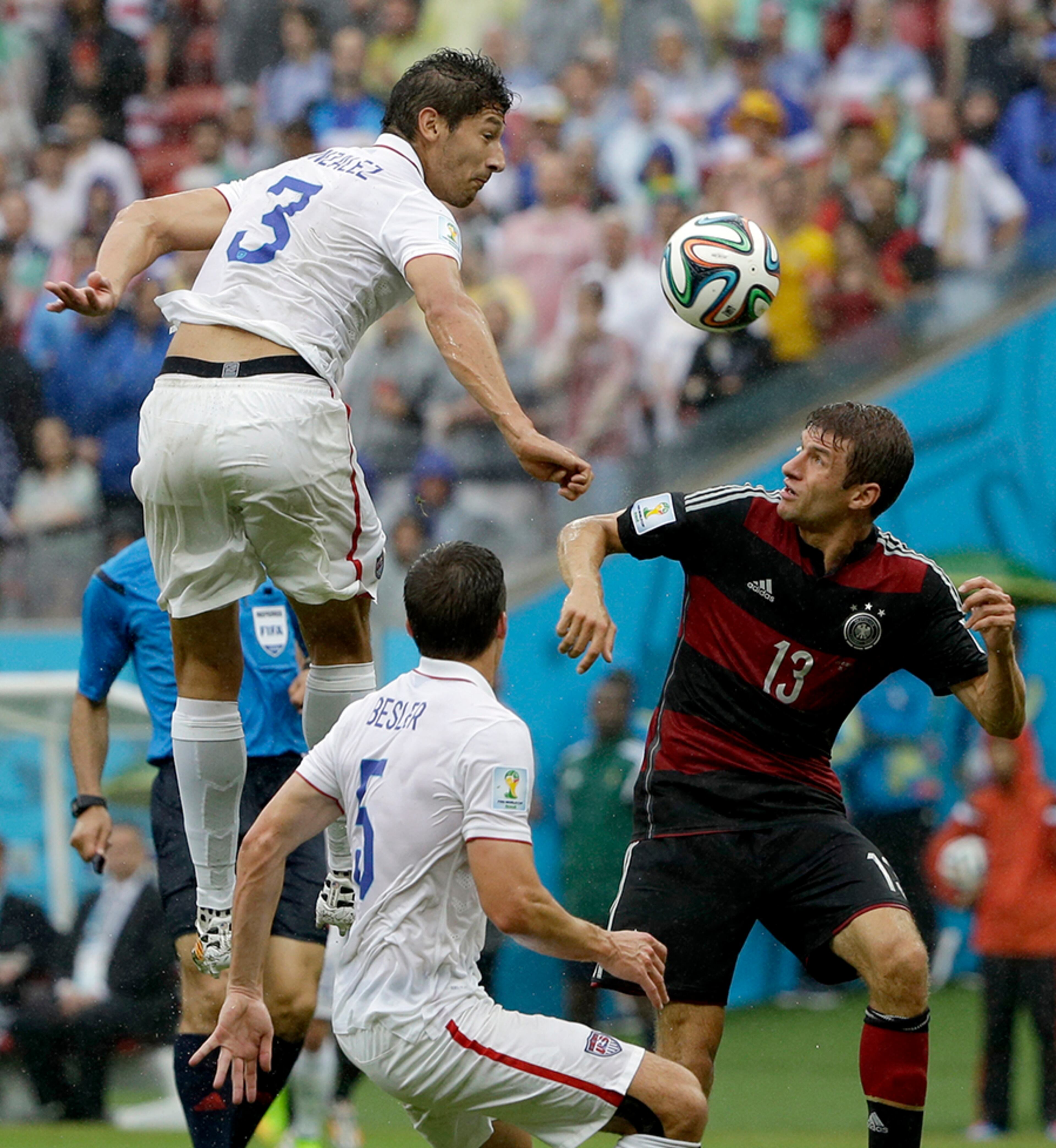 United States' Omar Gonzalez goes over Germany's Thomas Mueller to head the ball as United States' Matt Besler looks on during the group G World Cup soccer match between the USA and Germany at the Arena Pernambuco in Recife, Brazil, Thursday, June 26, 2014.