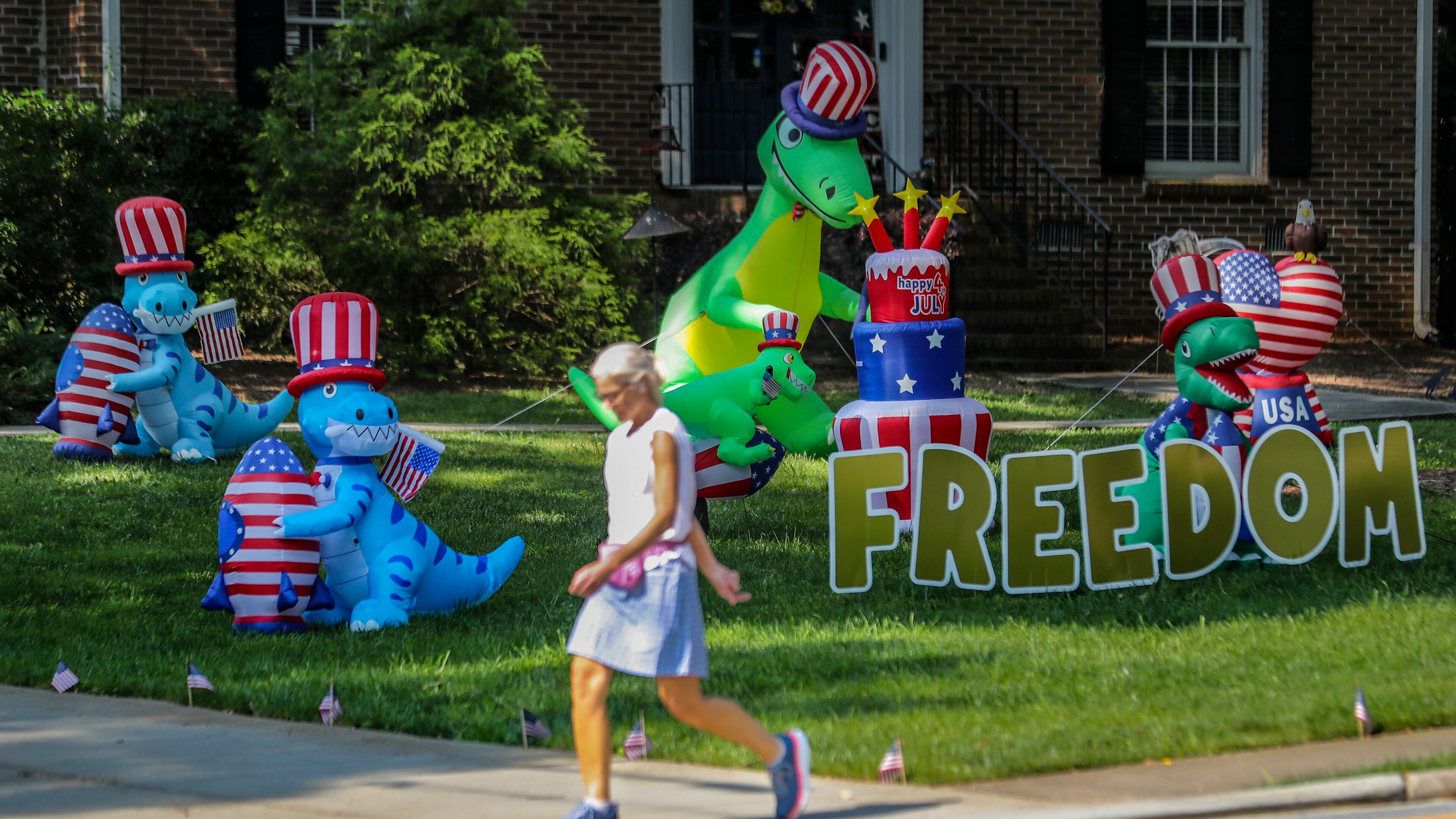 Alyson Cohen strolled by the display of dinosaurs on Dunwoody Club Drive near Braffington Court in Dunwoody on Friday, June 9, 2023. The display of dinosaurs first appeared in the neighborhood in 2020 then quickly evolved into holiday themed displays along with encouraging messages. (John Spink / John.Spink@ajc.com)