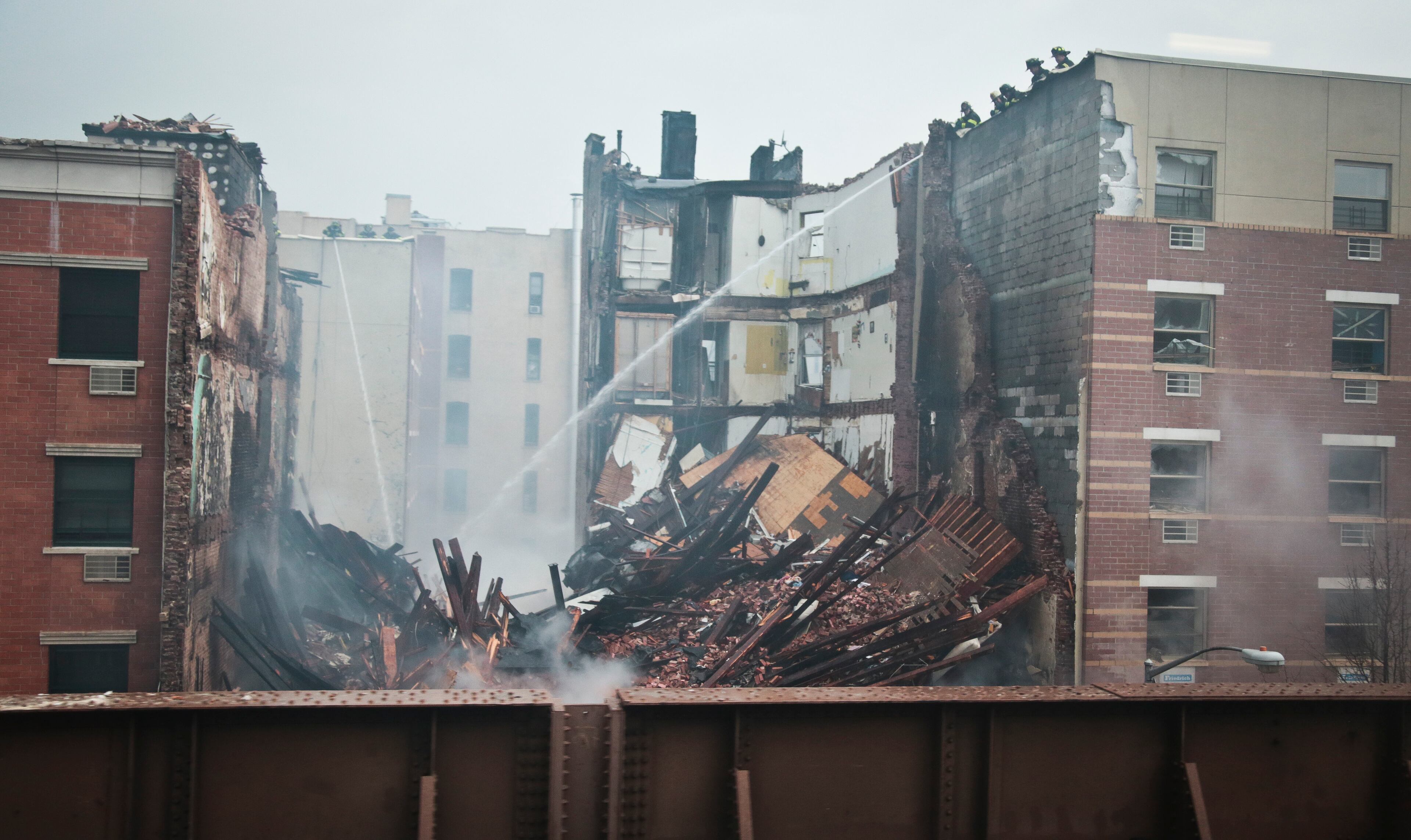 Firefighters continue to spray water on the smoldering debris from an explosion in Harlem, Wednesday, March 12, 2014 in New York. A gas leak triggered an explosion that shattered windows a block away, rained debris onto elevated commuter railroad tracks close by, cast a plume of smoke over the skyline and sent people running into the streets. (AP Photo/Bebeto Matthews)