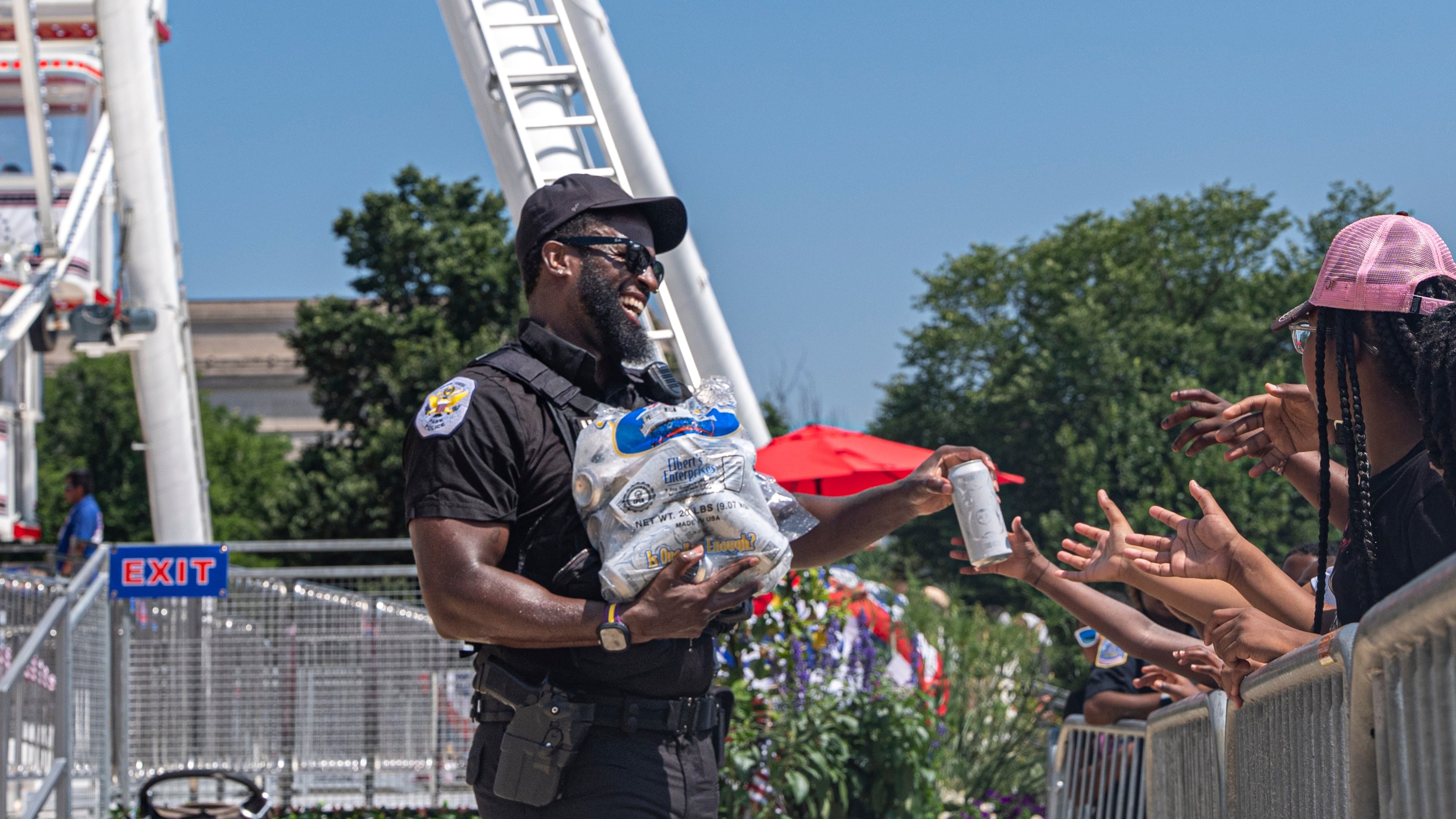 Children reach for cold bottles of water from U.S. National Park Police Officer R. Douglass as they wait in line for the ferris wheel at the Great American State Fair on the National Mall, Wednesday, July 1, 2026, in Washington. (AP Photo/Jen Golbeck)