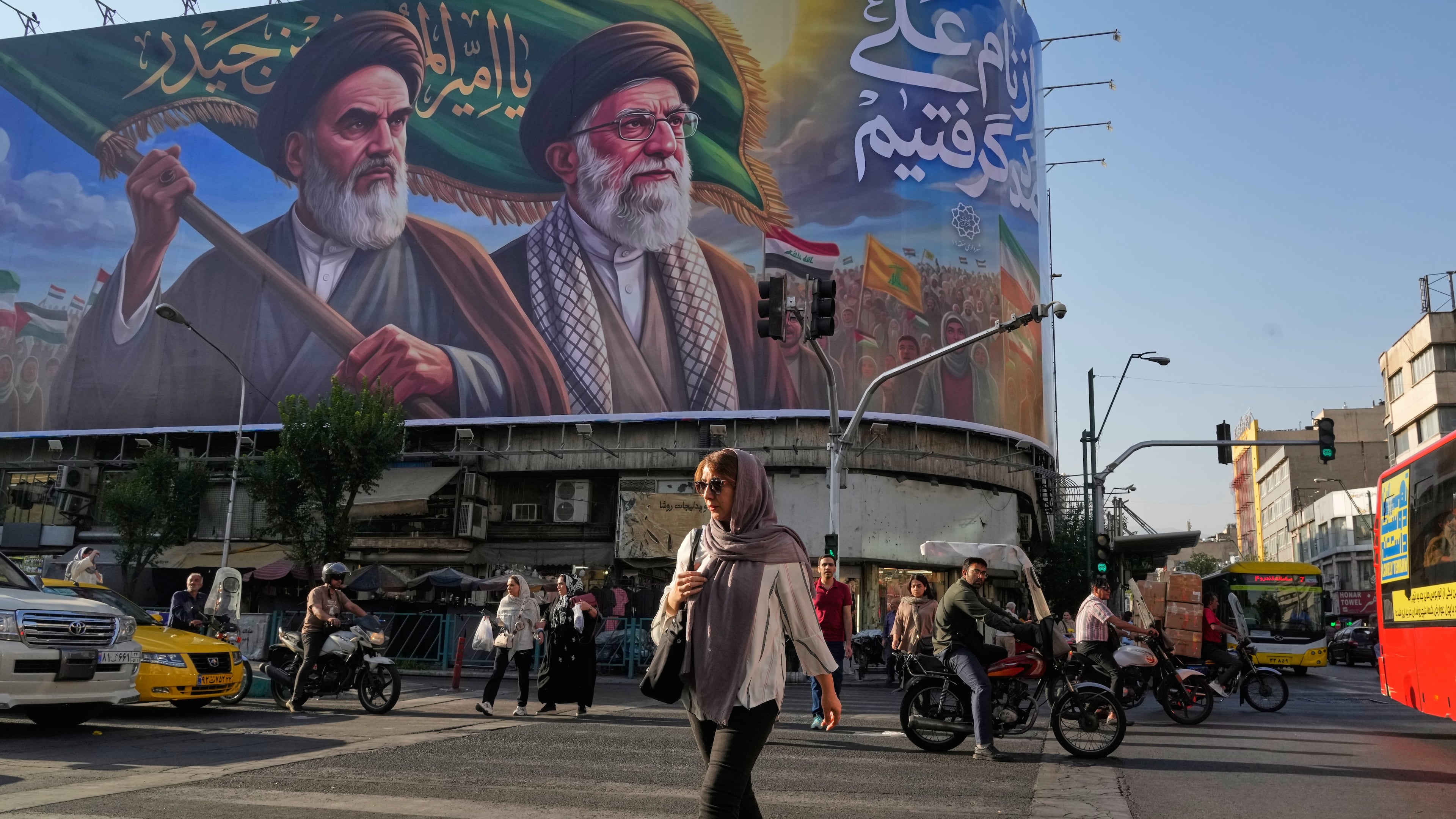 People walk under a banner showing portraits of the late revolutionary founder Ayatollah Khomeini, left, and the slain Supreme Leader Ayatollah Ali Khamenei, who was killed in U.S. and Israeli strikes on Feb. 28, in Tehran, Iran, Saturday, June 6, 2026. (AP Photo/Vahid Salemi)