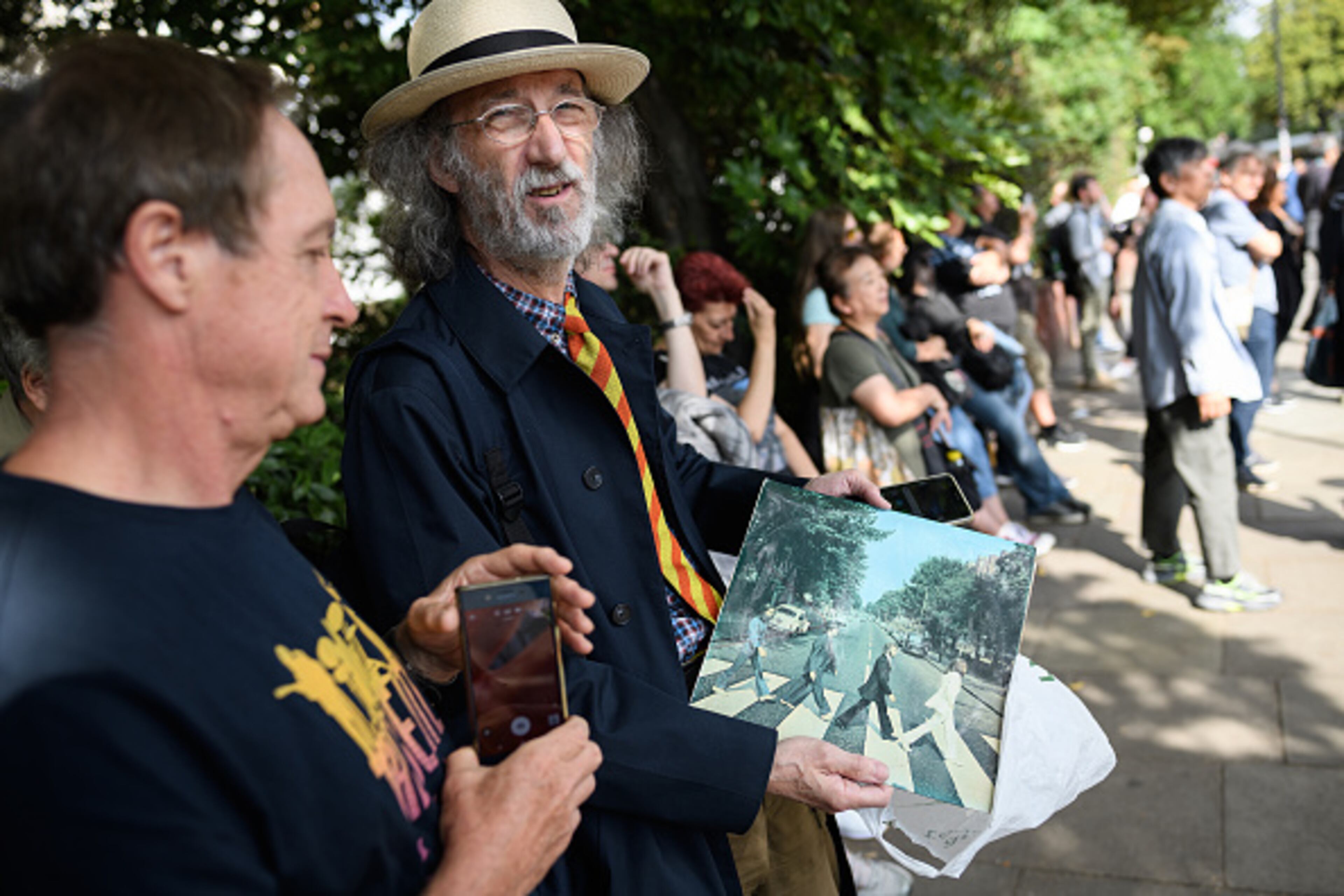 LONDON, ENGLAND - AUGUST 08: A man holds his original copy as members of the public recreate the iconic album cover for the Beatles album "Abbey Road" on the same pedestrian crossing, fifty years since it was taken, on August 08, 2019 in London, England. The zebra crossing is just outside the recording studios and has become a popular location for music fans visiting London. (Photo by Leon Neal/Getty Images)