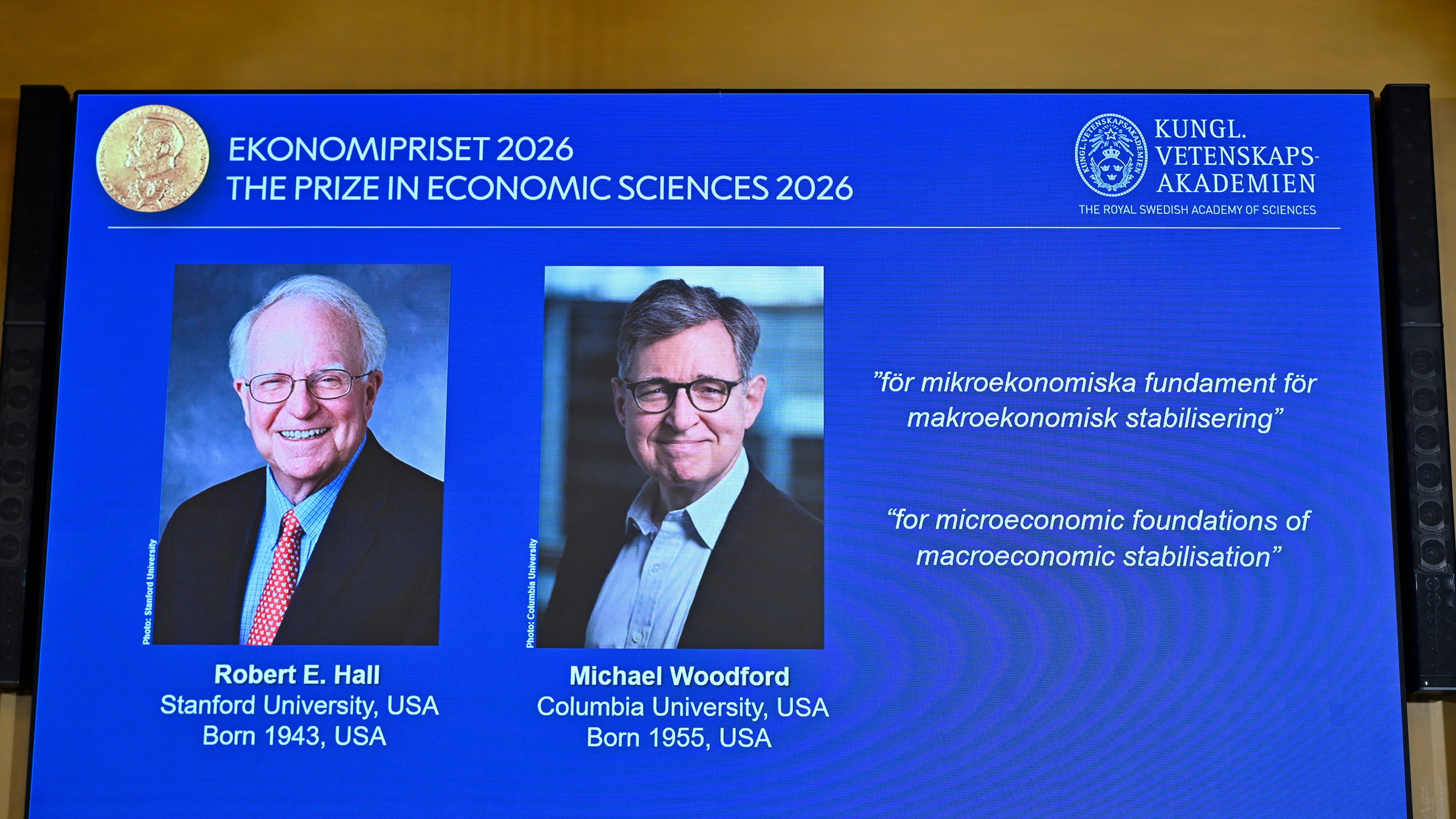 Portraits of Robert E. Hall and Michael Woodford are shown on the screen as they are announced as the laureates of the Sveriges Riksbank Prize in Economic Sciences in Memory of Alfred Nobel at the Royal Swedish Academy of Sciences in Stockholm, Sweden, Monday, Oct. 12, 2026. (Anders Wiklund/TT News Agency via AP)