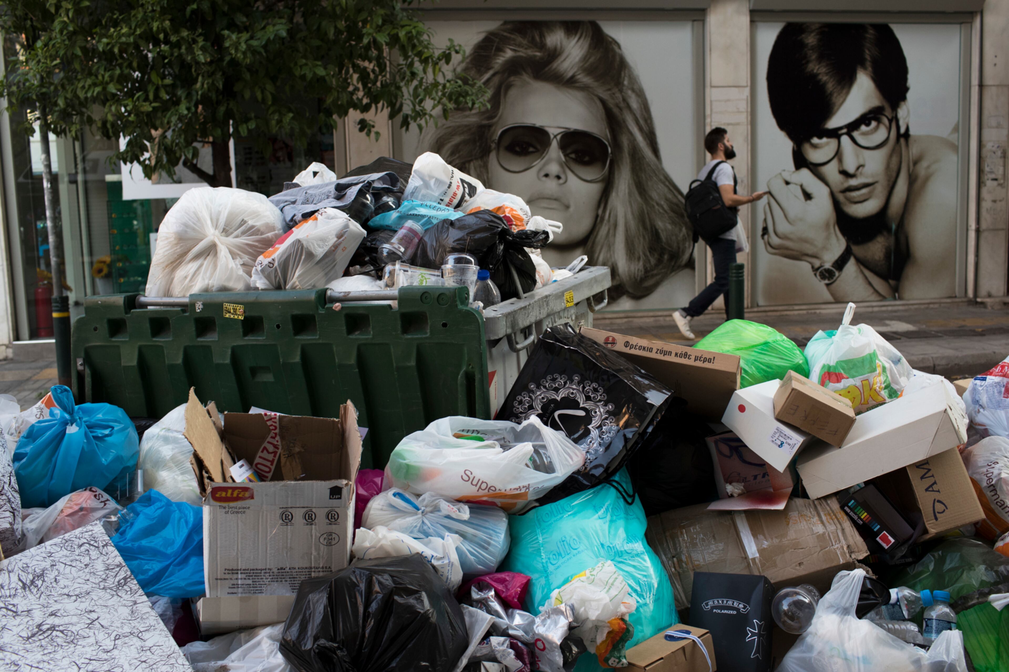 A man walk next an optical shop behind a pile of garbage in Piraeus, near Athens, on Monday, June 26, 2017. Municipality workers have been on strike for almost a week, hindering trash collection across the country. (AP Photo/Petros Giannakouris)