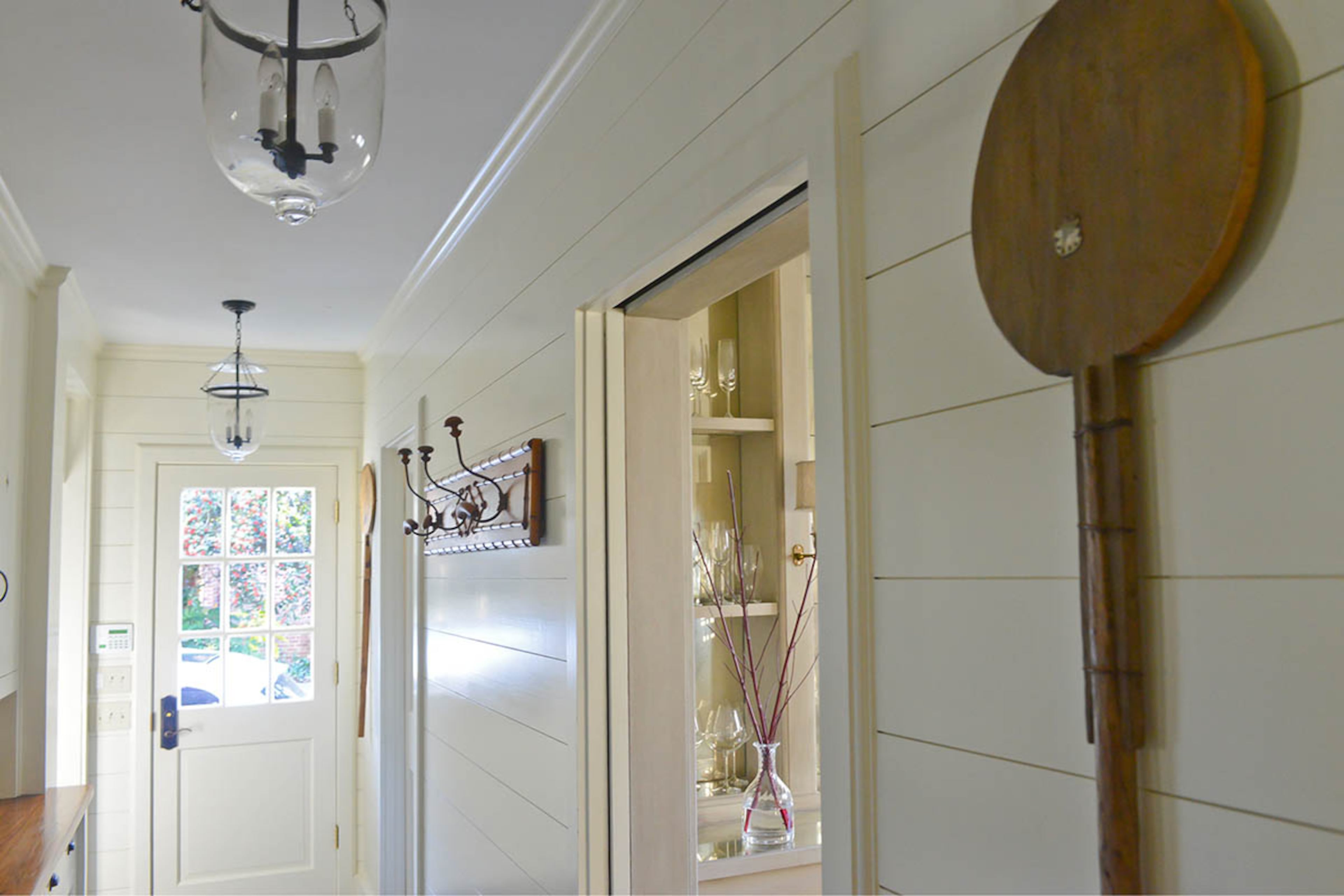 The side entry is stylish and functional. Hooks and cabinets make the space a great mudroom, and shiplap gives it cottage charm. Bell jar light fixtures and a vintage pizza paddle complete the look.