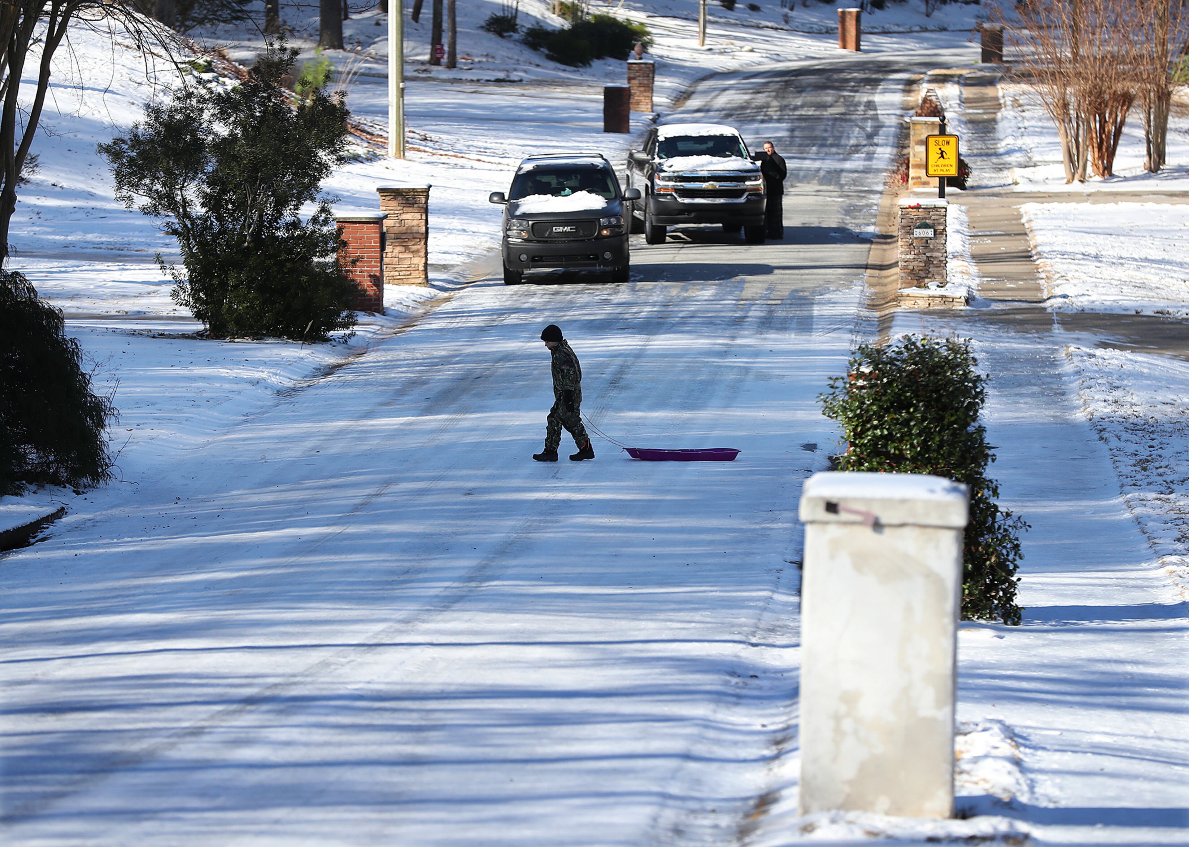 January 8, 2017, Canton: Chase Collins, 8, carefully crosses ice covered Pine Terrace Road with his sled after a trip down the road while a pair of motorist decide if they want to risk trying to drive up the hill in Cherokee Falls Estates at the Lake subdivision in the aftermath of the storm on Sunday, Jan. 8, 2017, in Canton. Several crashes occured in the area and multiple vehicles were left abandoned after getting stuck on the ice. Curtis Compton/ccompton@ajc.com