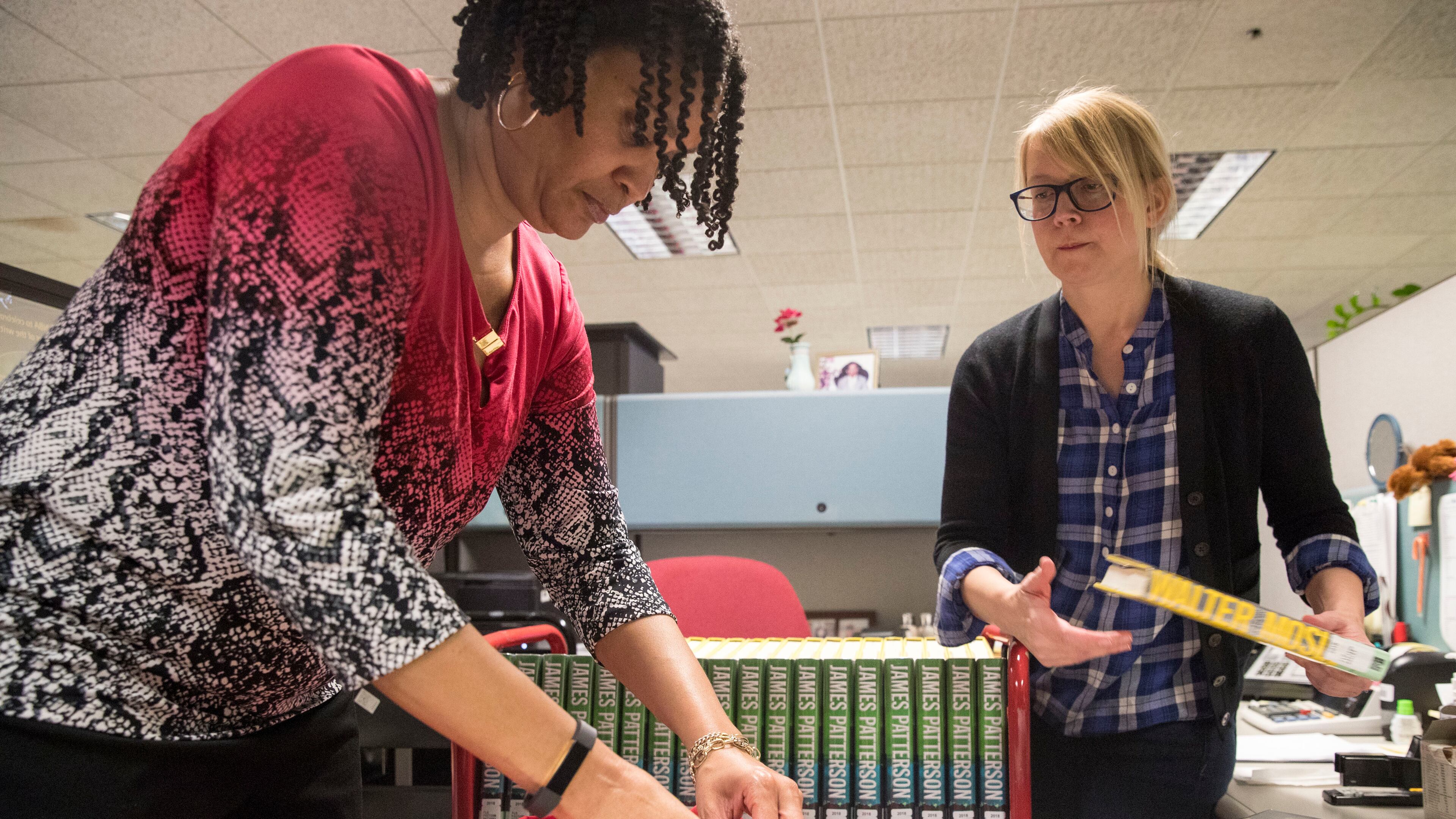 Virginia Collier, right, manager of collections management and technical services at Atlanta Central library, and Charmaine Johnson, assistant manager of collections management and technical services, prepare a leased Walter Mosley novel for distribution at Atlanta Central Library. ALYSSA POINTER/ALYSSA.POINTER@AJC.COM