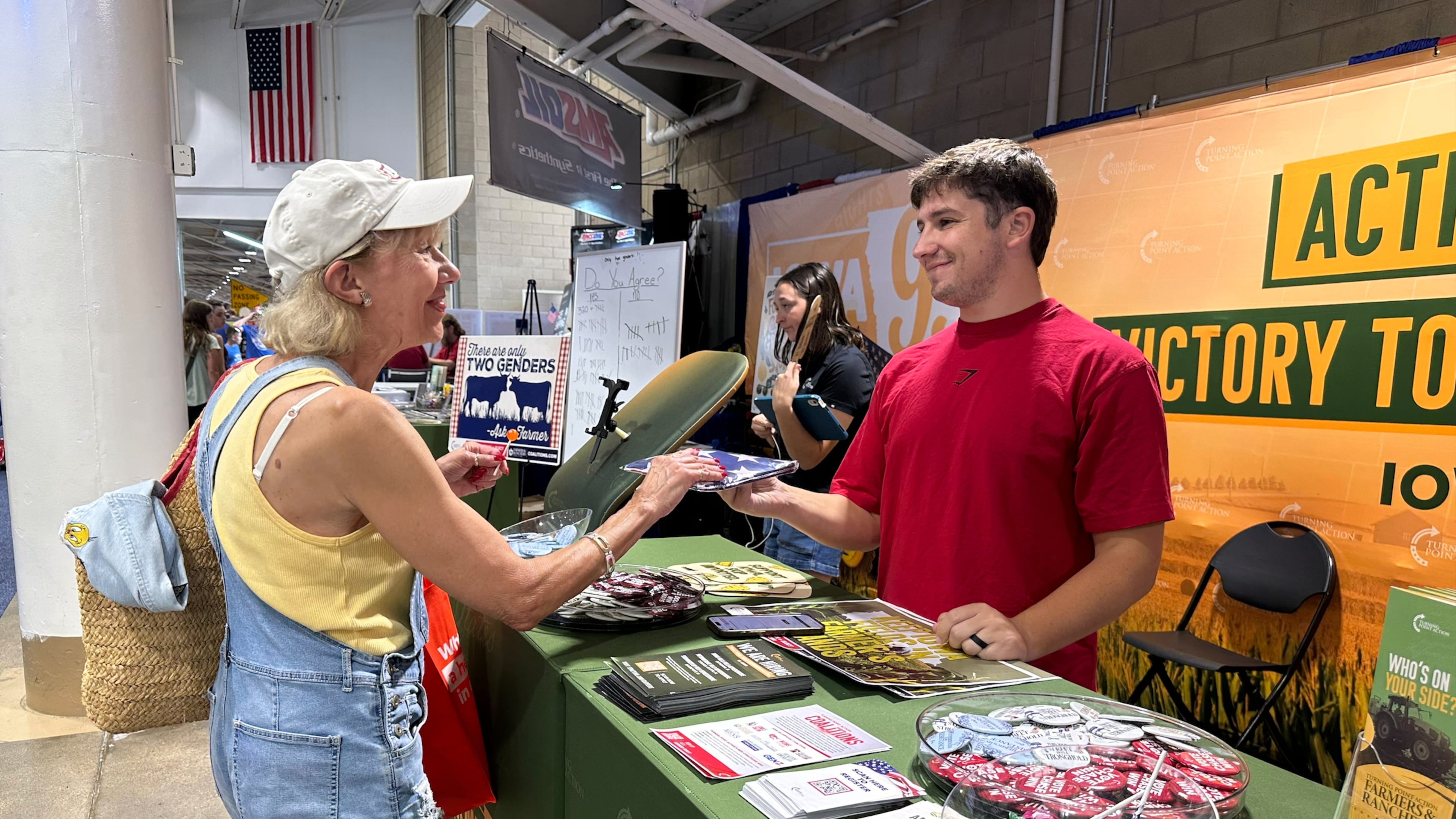 A Turning Point Action staffer gives an American flag to a voter at the Iowa State Fair in Des Moines, Iowa, Friday, Aug. 21, 2026. (AP Photo / Hannah Fingerhut)