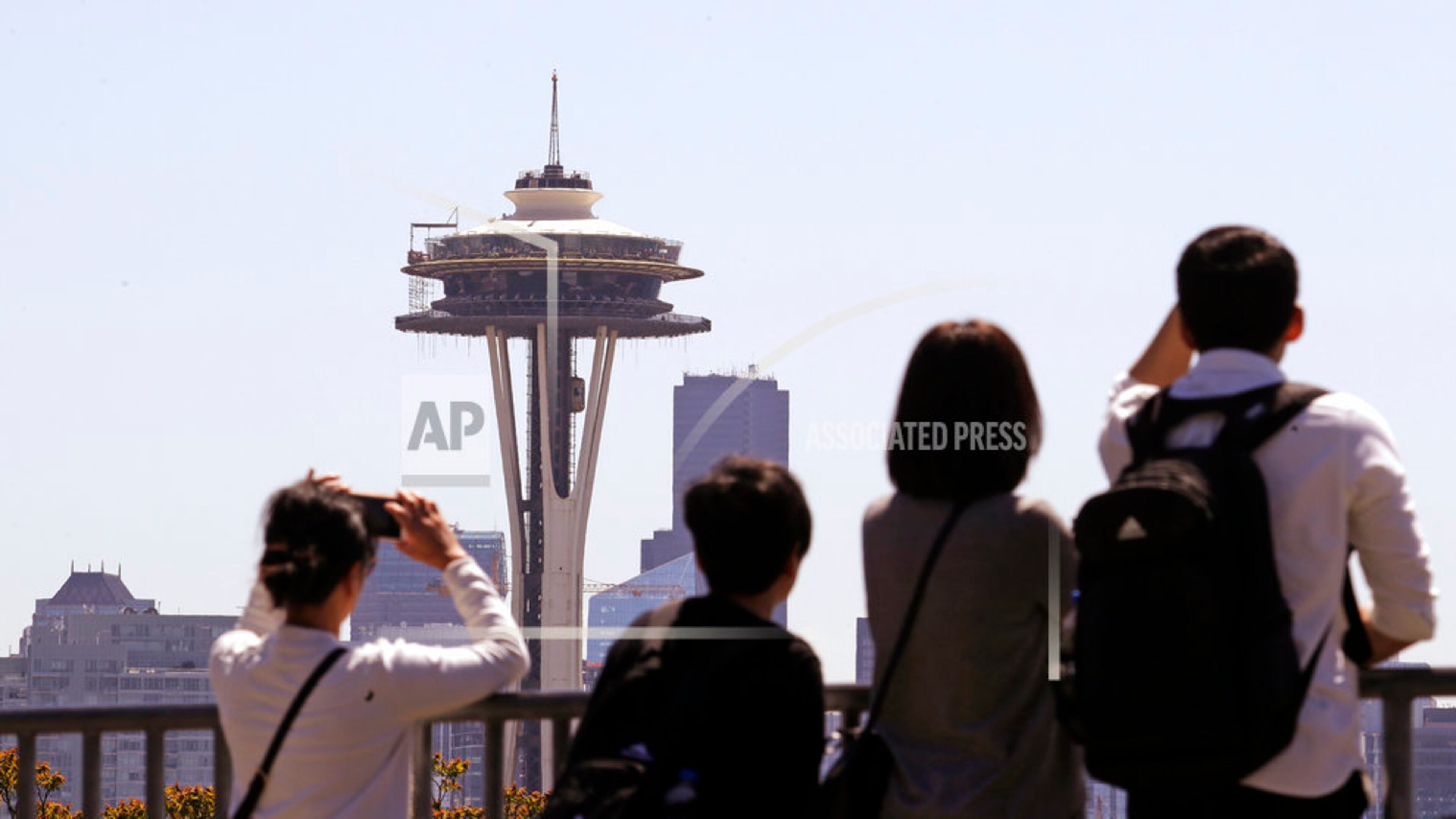 Tourists look across at the Space Needle, where a floor of scaffolding remains below the upper portion, in Seattle on Tuesday, May 22, 2018. The family-owned landmark is set to unveil the biggest renovation in its 56-year history next month, a $100 million investment in a single year of construction that transformed the structure's top viewing level some 500-feet above ground. (AP Photo/Elaine Thompson)