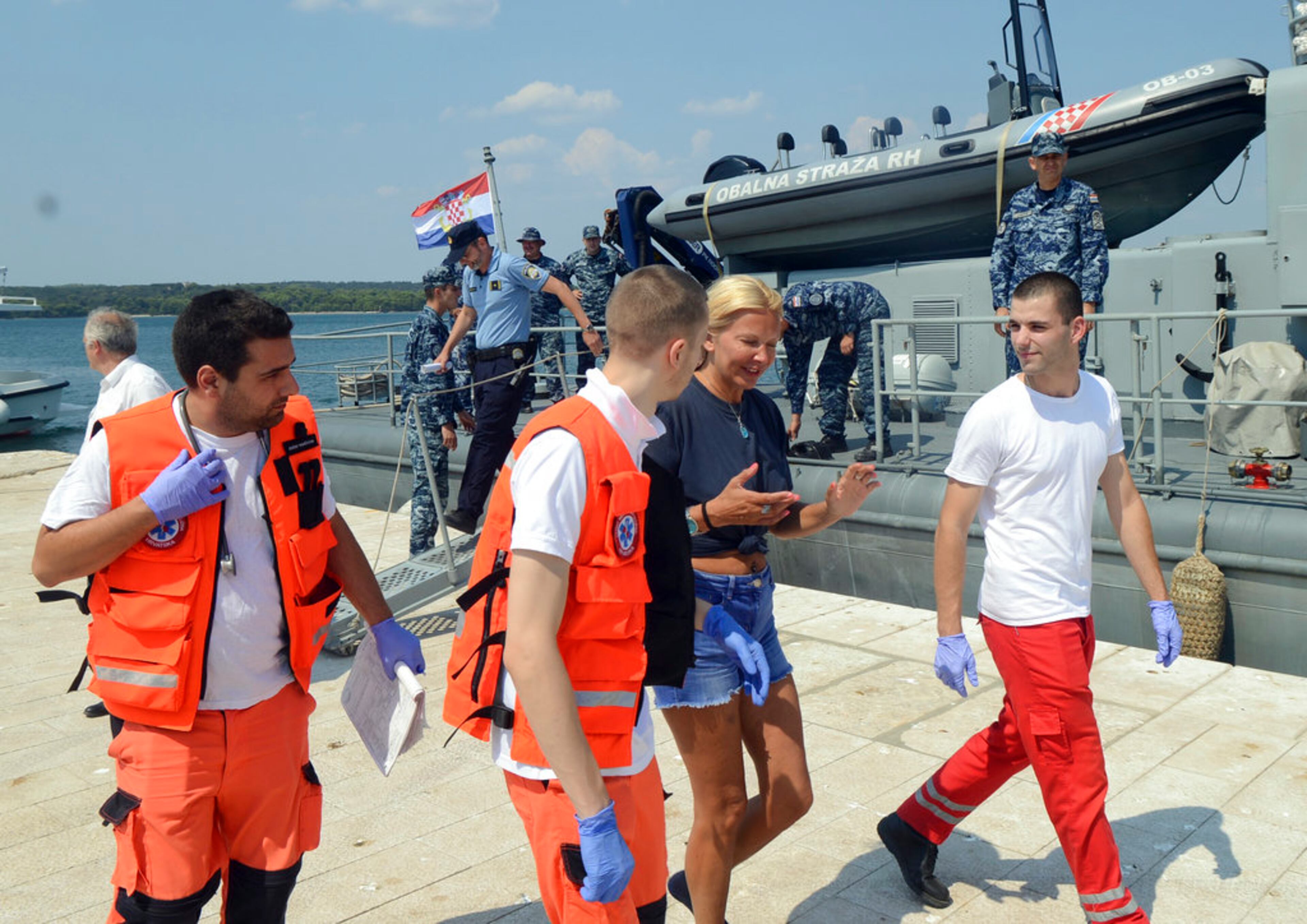 In this photo taken Aug. 19, 2018, a woman who identified herself as Kay from England, center, is escorted by rescuers from a Croatian Coast Guard vessel in the port in Pula, Croatia. A British woman was rescued Sunday after falling from a cruise ship and spending 10 hours in the Adriatic Sea at night, Croatia's coast guard said. (AP Photo)