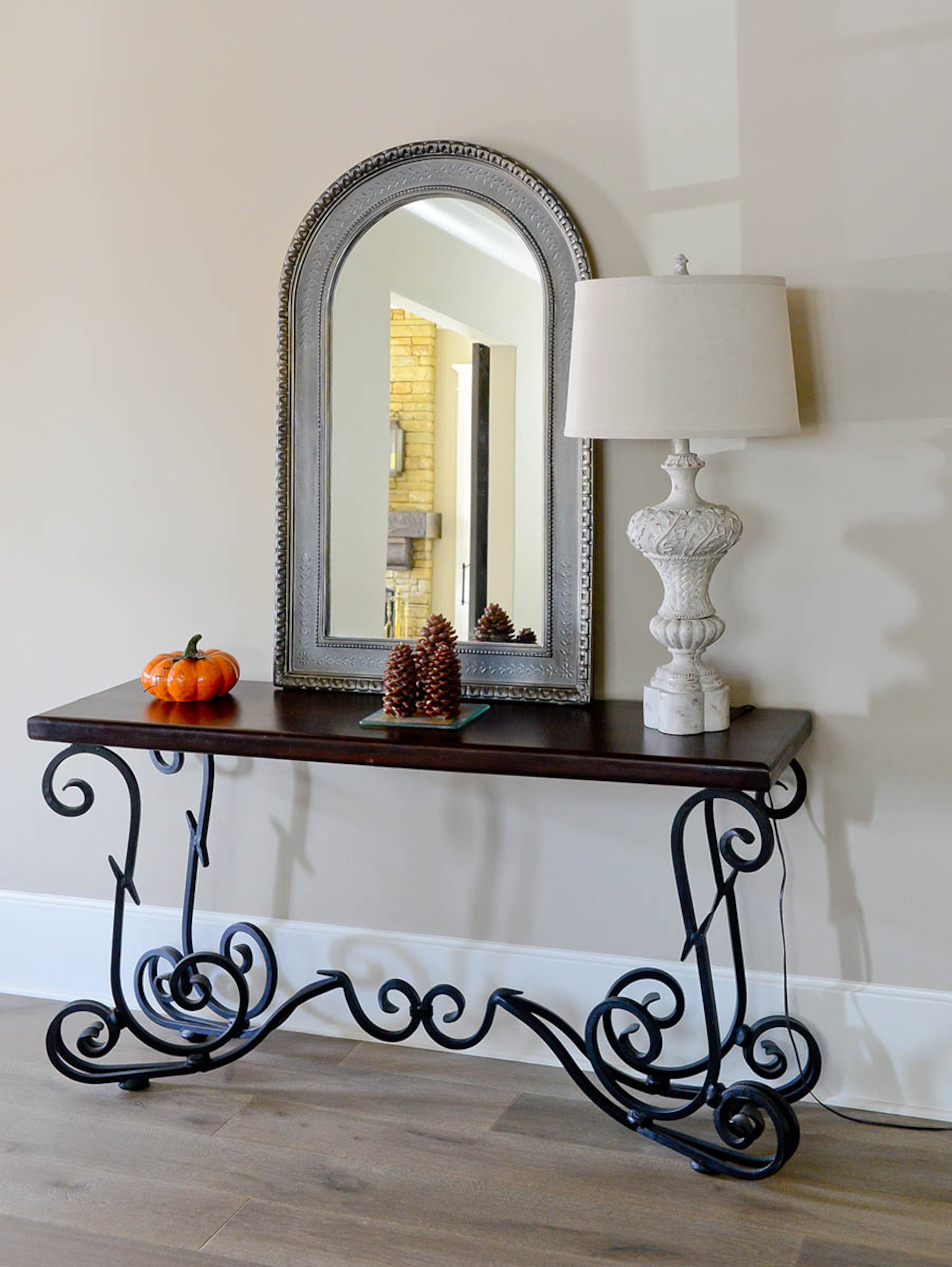 A mirror propped on a console table with a lamp creates a welcoming vignette in the Roswell home. Placed near the entry, small trinkets like pumpkin and pinecone accessories can easily be changed with the season.