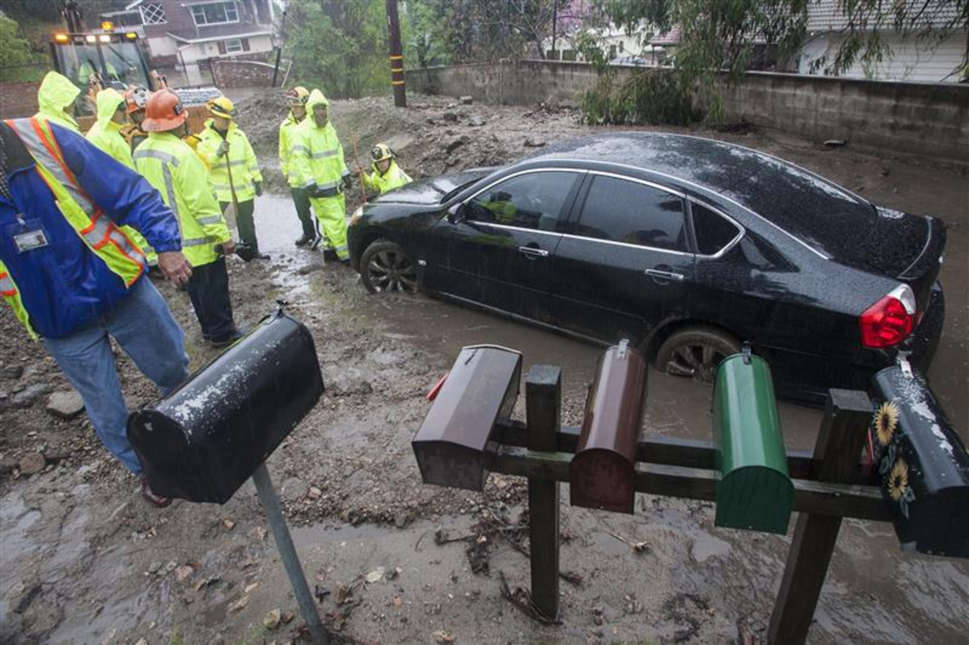 Workers try to help a woman to get her car unstuck from the mud brought by the rain along a hillside in Glendora, Calif., Friday, Feb. 28, 2014. The first wave of a powerful Pacific storm spread rain and snow early Friday through much of California, where communities endangered by a wildfire just weeks ago now faced the threat of mud and debris flows. (AP Photo/Ringo H.W. Chiu)