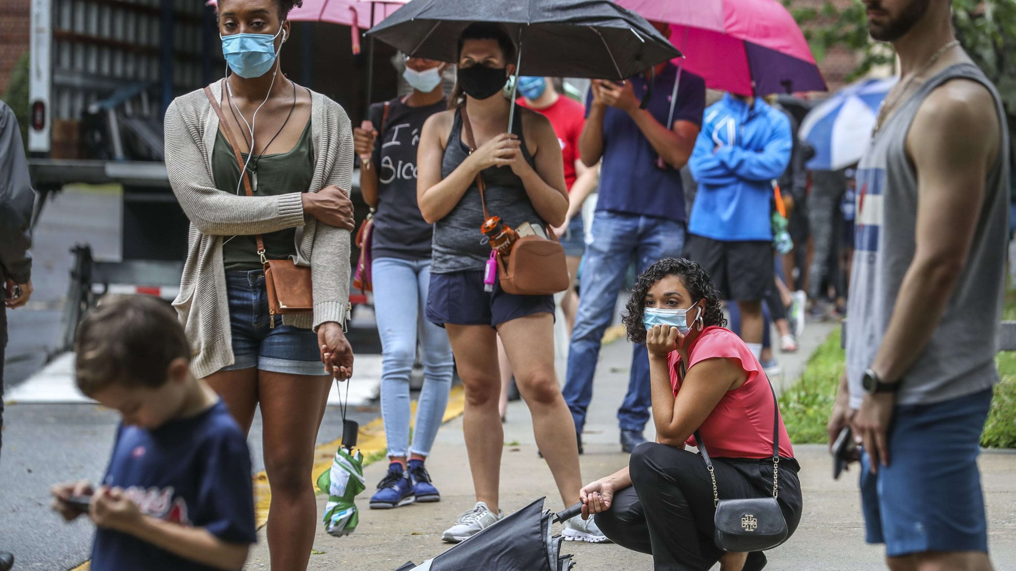 Stephanie Herrera crouches in line as she and other voters lined up in the rain on Friday, June 6, 2020 at Garden Hills Elementary School located at 285 Sheridan Dr NE, in Atlanta where the wait for early voting was between one and two hours. JOHN SPINK/JSPINK@AJC.COM