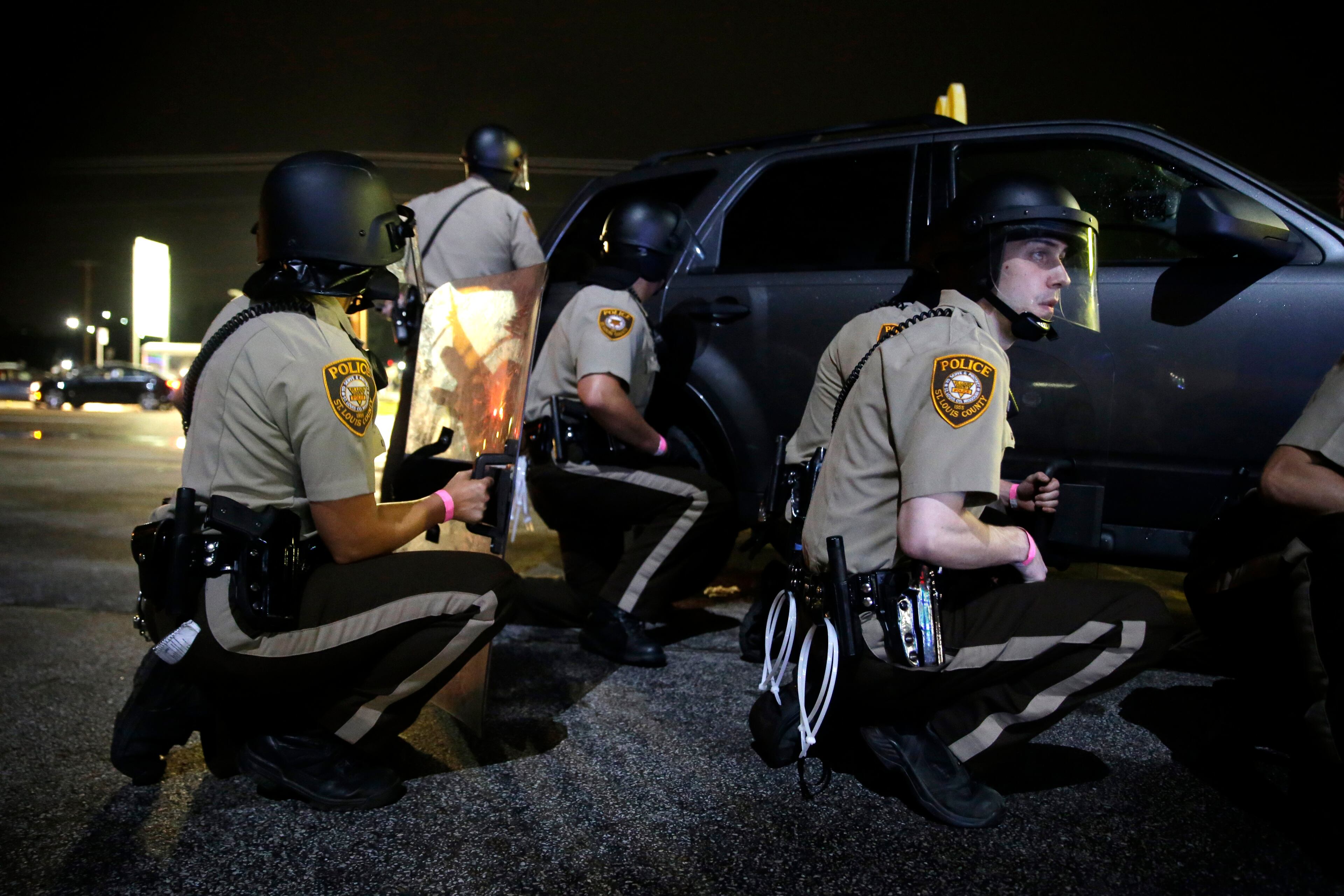 Police take cover after gunfire near a protest in Ferguson, Mo., Sunday, Aug. 9, 2015. The one-year anniversary of Michael Brown's death in Ferguson began with a march in his honor and ended with a protest that was interrupted by gunfire. (AP Photo/Jeff Roberson)