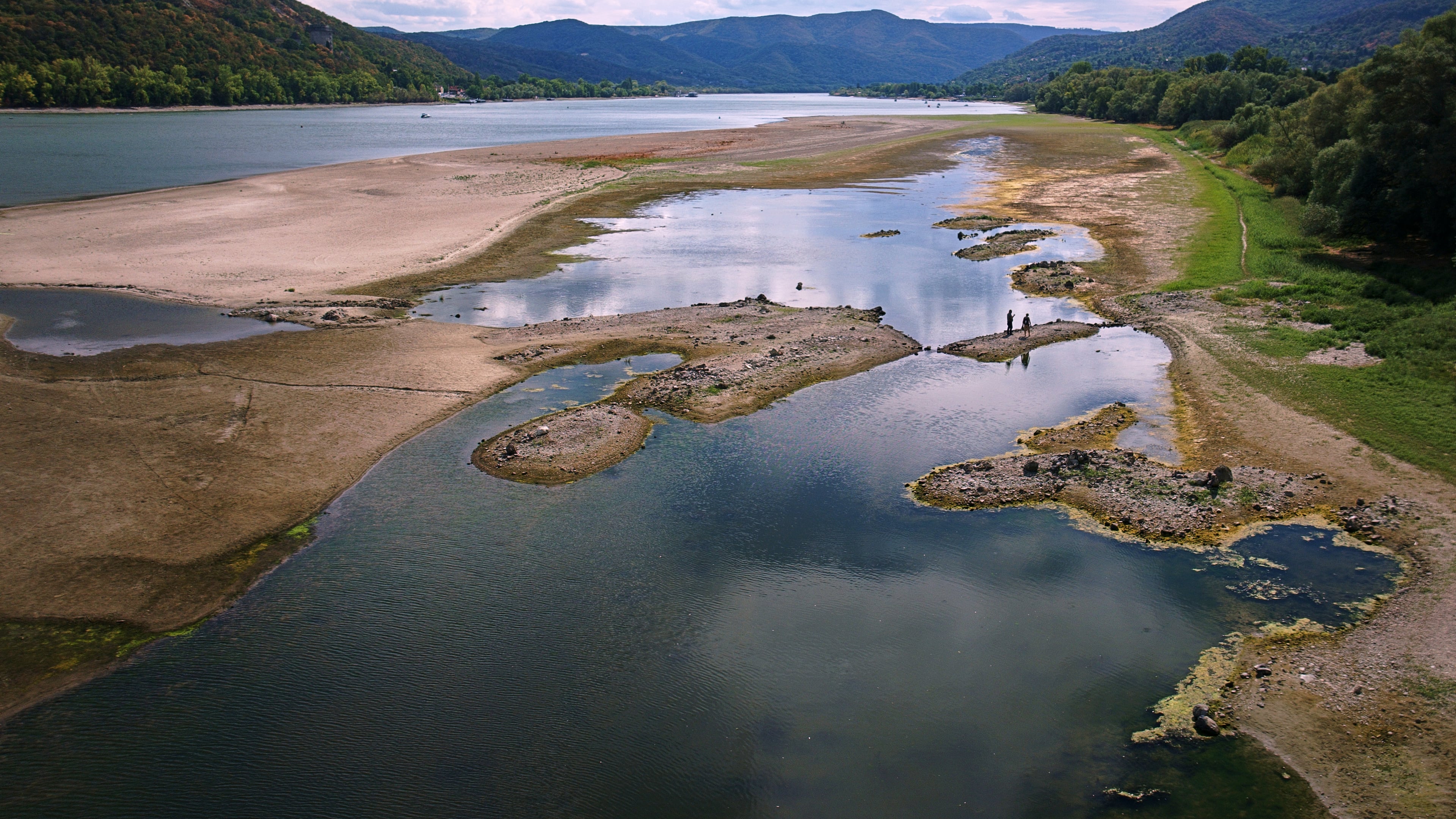 People walk on sandbanks exposed by record-low water levels in the Danube River after drought and extreme heat near Nagymaros, Hungary, on Aug. 18, 2026. (AP Photo/Bela Szandelszky)
