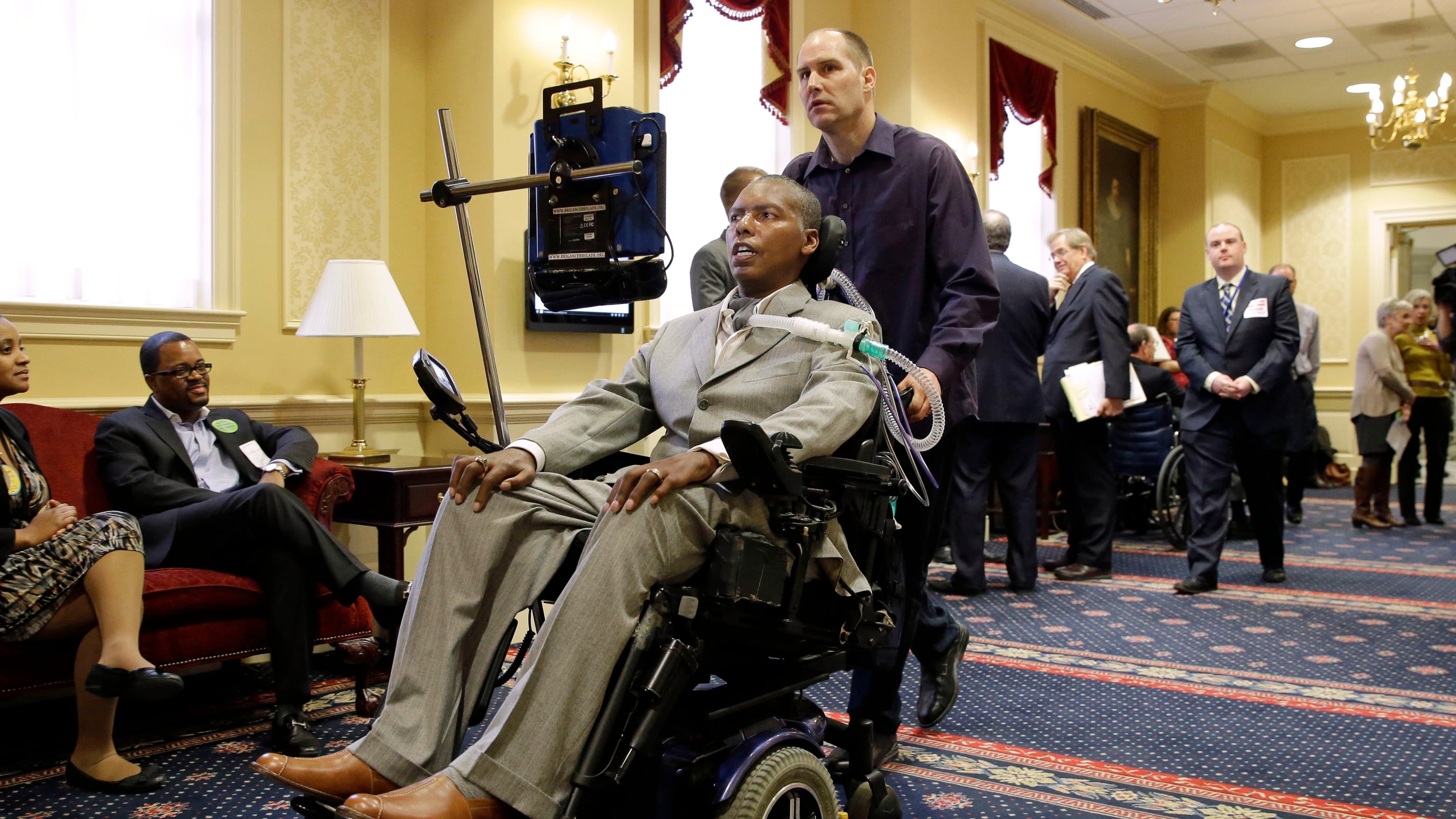FILE - Former Baltimore Ravens NFL football player O.J. Brigance, center, current senior advisor to player development, is pushed by a nurse outside of a committee room in Annapolis, Md., March 10, 2015, after testifying to Maryland lawmakers against a right-to-die bill. (AP Photo/Patrick Semansky, File)