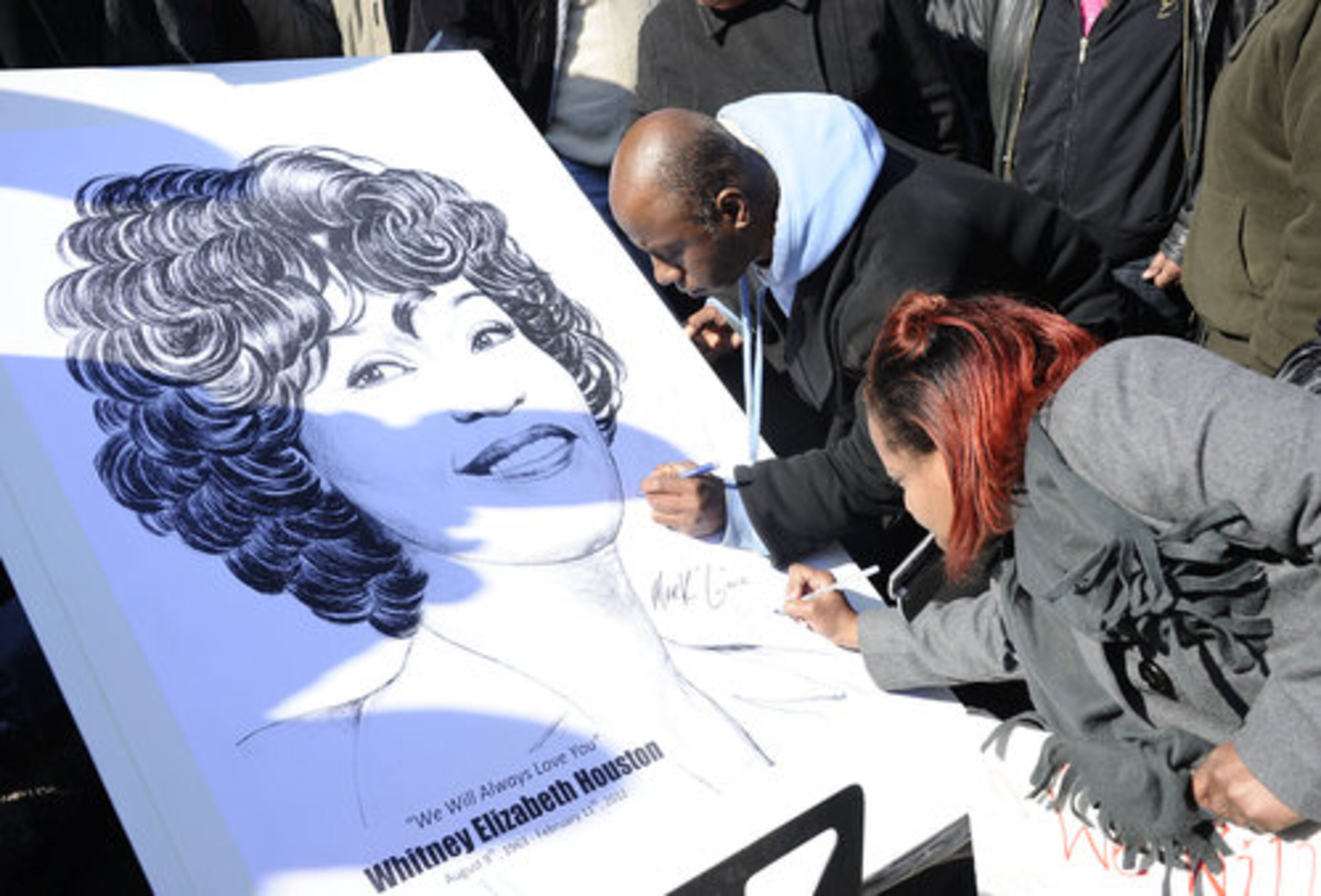 Fans sign a poster showing a picture of Whitney Houston near a funeral service for the singer at the New Hope Baptist Church in Newark, N.J., Saturday, Feb. 18, 2012.