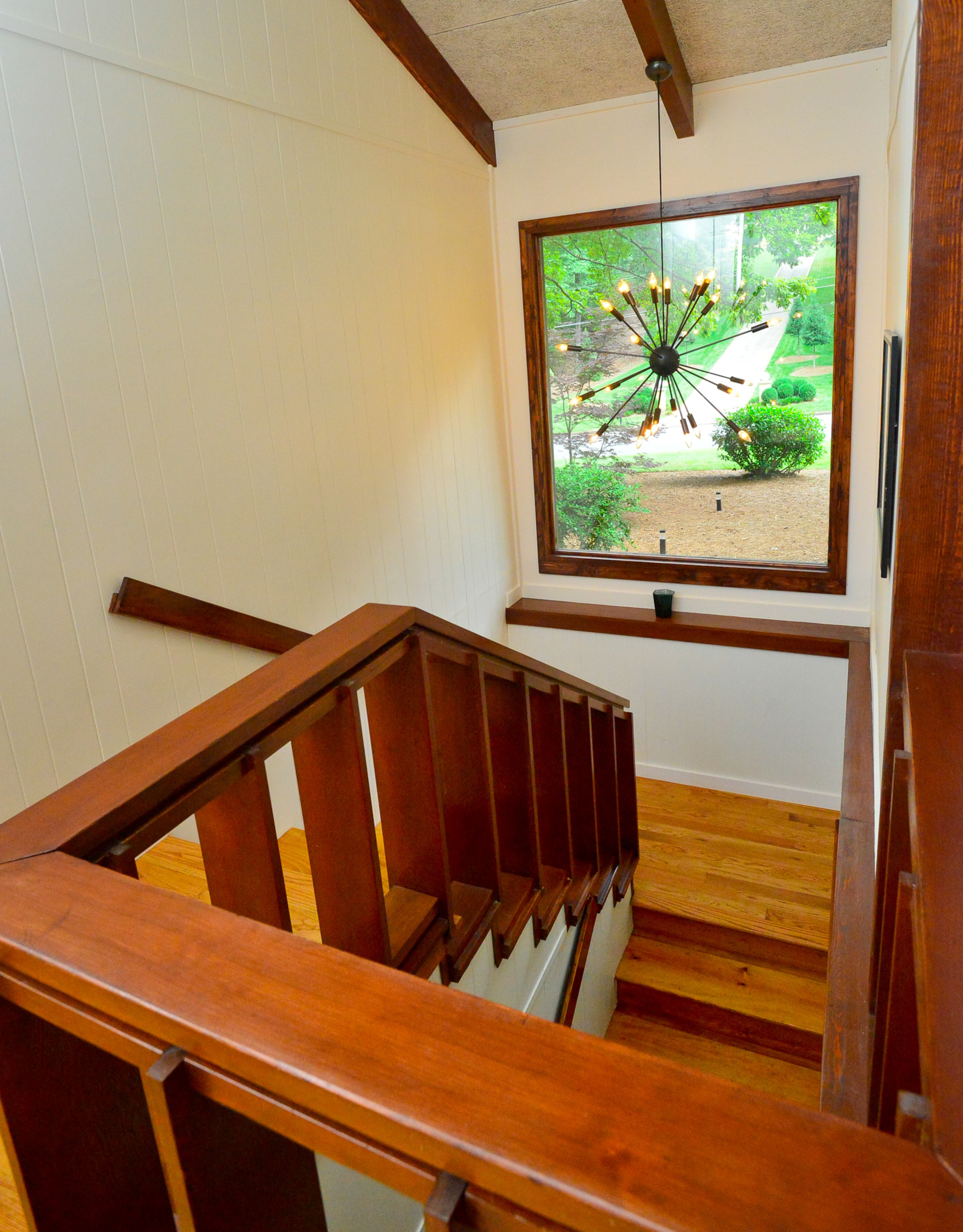 The renovated stairwell is rich with chunky wood railings and beams. The stairs are lit by natural light during the day and a chandelier from Design Within Reach at night.