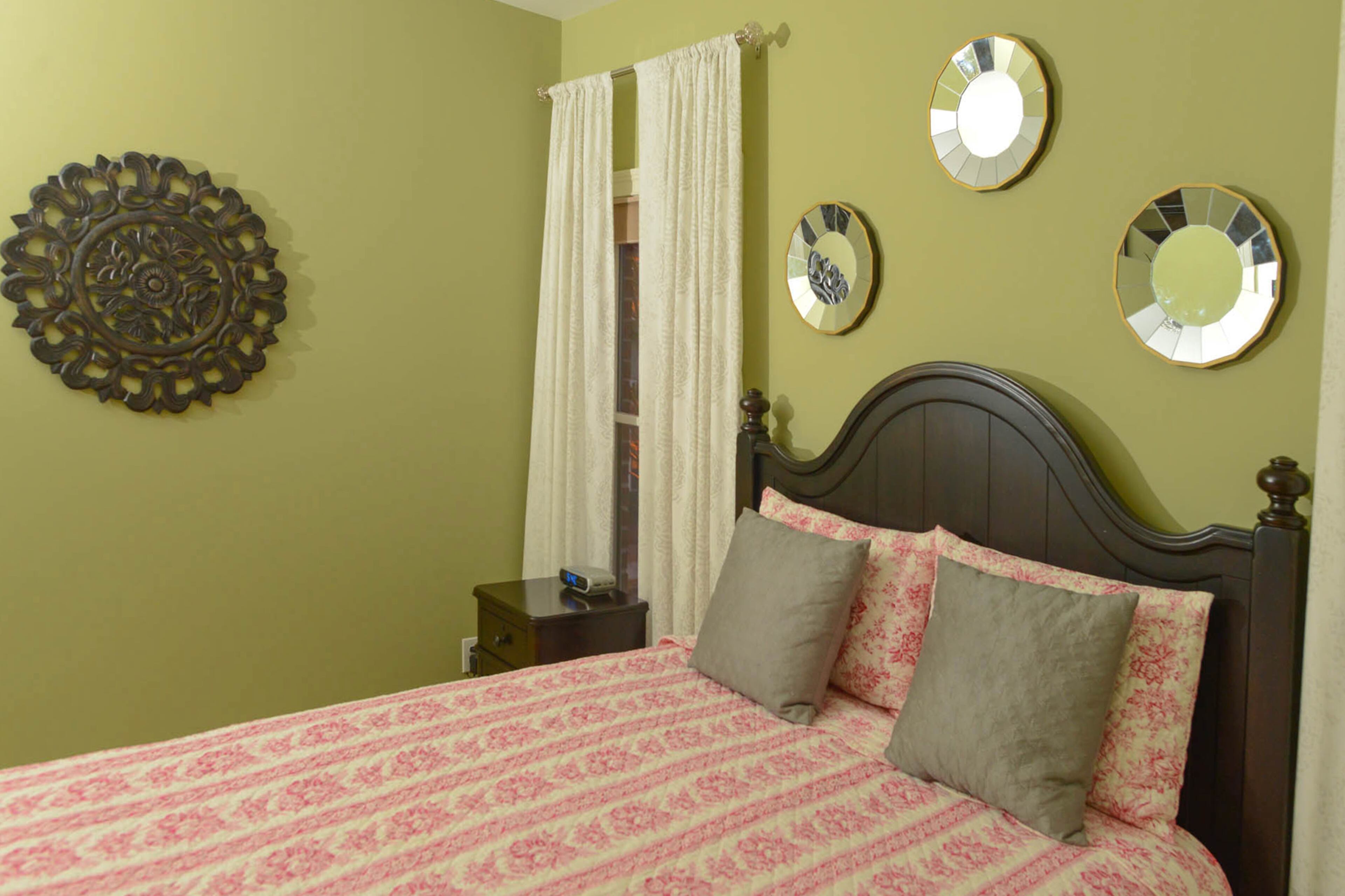 A trio of mirrors shine above the wood bed in the pink-and-green guest bedroom. Callahan likes using different materials, like the iron and mirrored wall art, in her transitional home decor.