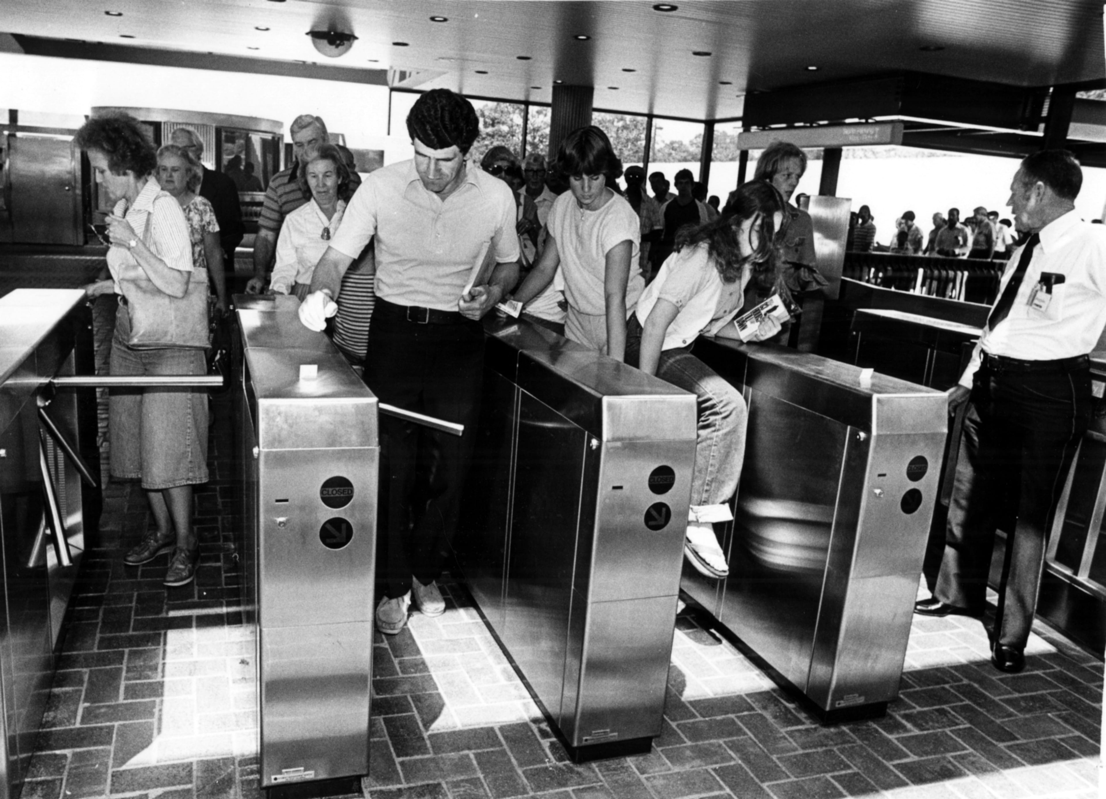 Original caption: "June 30, 1979 - The first passengers come through, or like the girl on right, climb over, the fare gates. Some of the turnstiles stuck and people had to step over them to get in while they were trying to be repaired."
