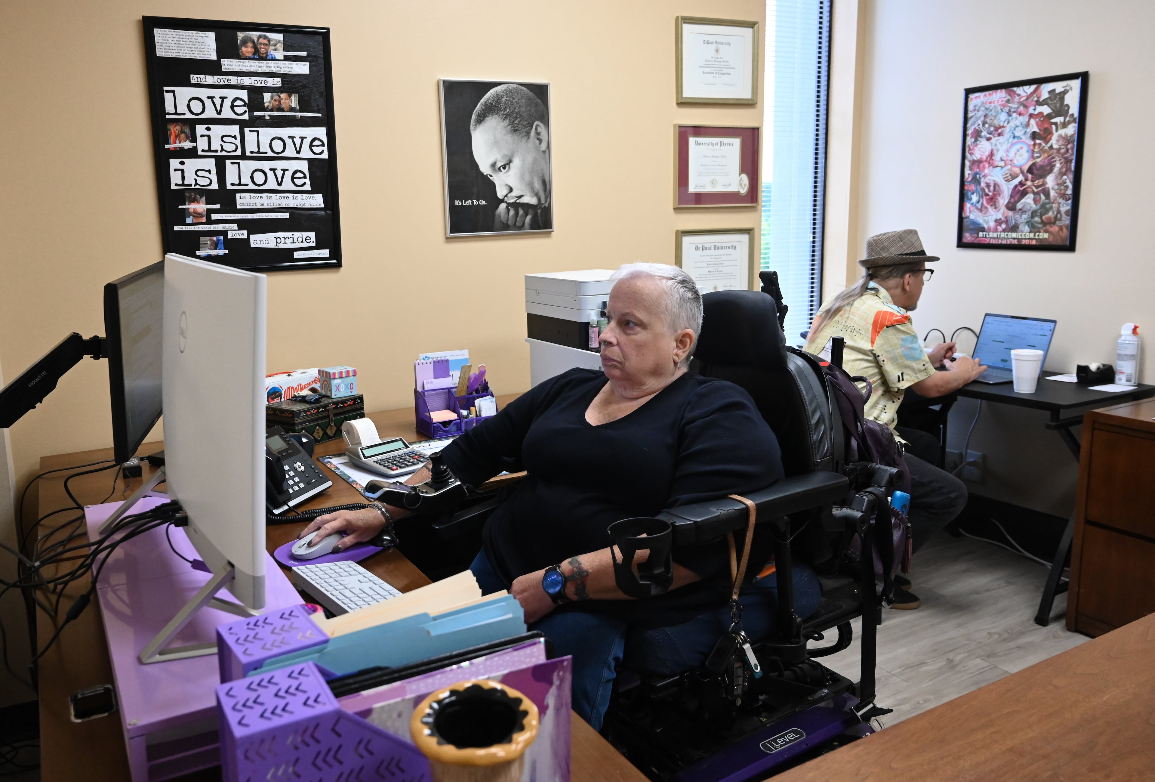 Rebecca Ramage-Tuttle, assistant director of the Statewide Independent Living Council of Georgia, checks her emails, as her husband and volunteer George Tuttle sits behind her desk at the SILCGA office, Thursday, July 10, 2025, in Decatur. (Hyosub Shin/AJC)
