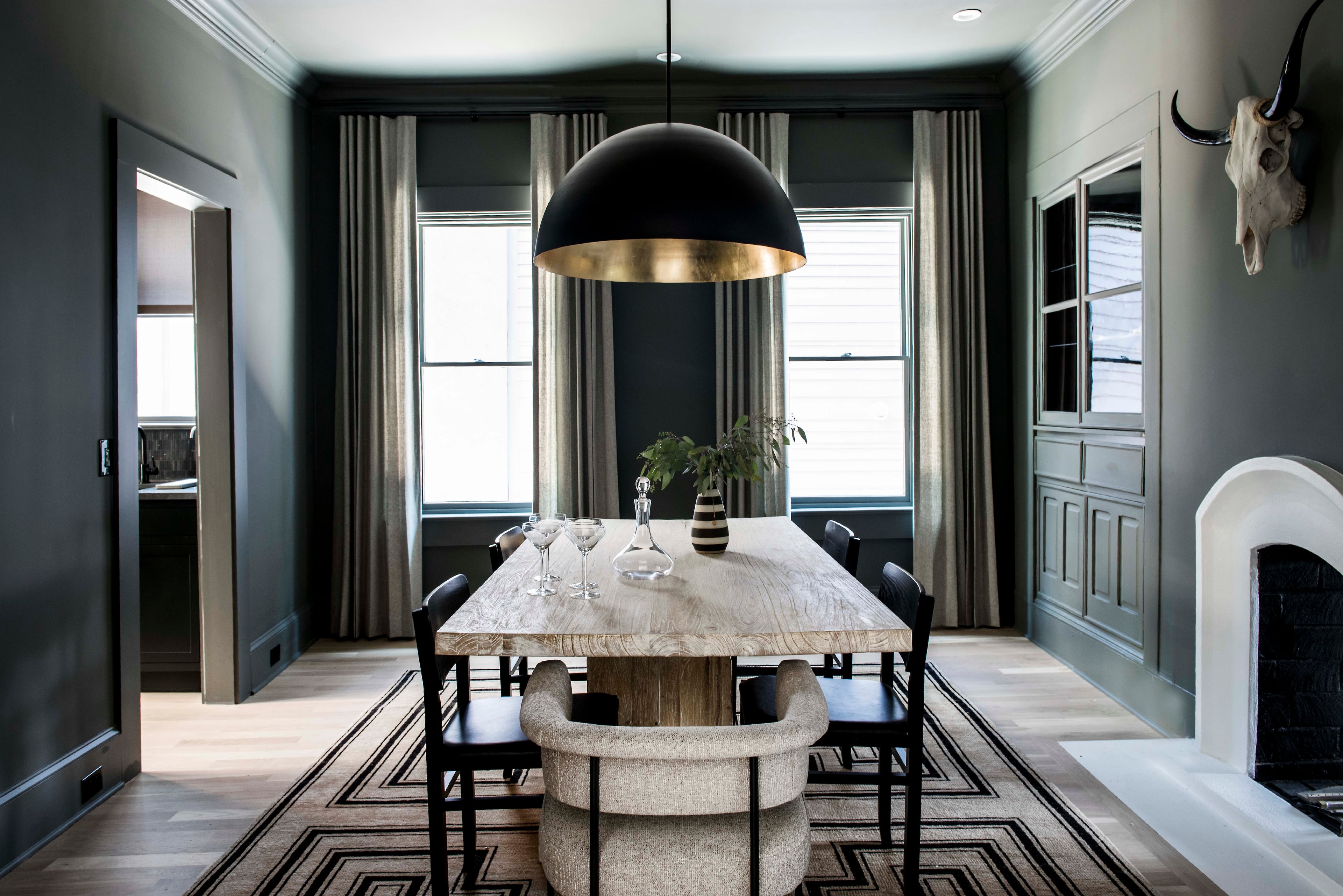 The dining room was painted on all sides for a jewel box effect that cloaks the room in a dramatic shade of Benjamin Moore Amherst Gray. Sweeping window treatments from The Shade Store make use of the high ceilings, while a bowl-shaped Circa pendant light over the Noir dining table draws the eye. Text by Lori Keong/Photo by Dominique White
