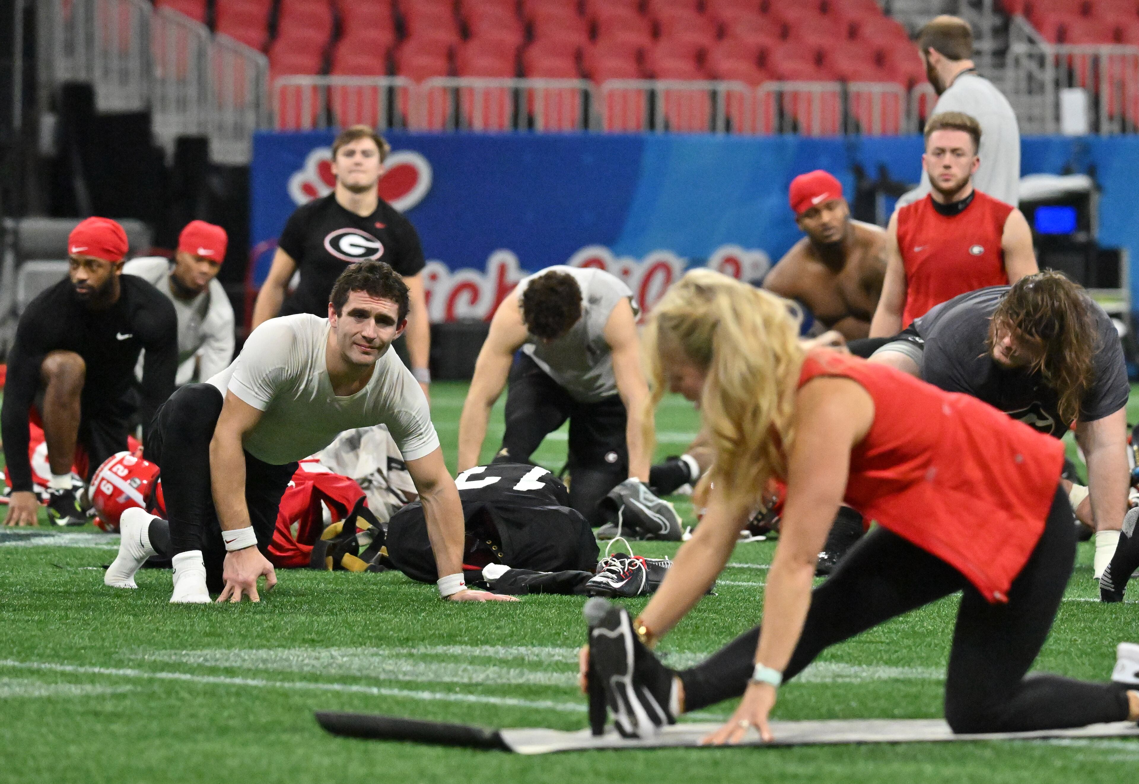 Georgia's quarterback Stetson Bennett (left) looks as an instructor (foreground) leads a stretch session for Georgia players during a practice session for the Chick-fil-A Peach Bowl game against Ohio State at the Mercedes-Benz Stadium on Thursday, Dec. 29, 2022, in Atlanta. (Hyosub Shin / Hyosub.Shin@ajc.com)