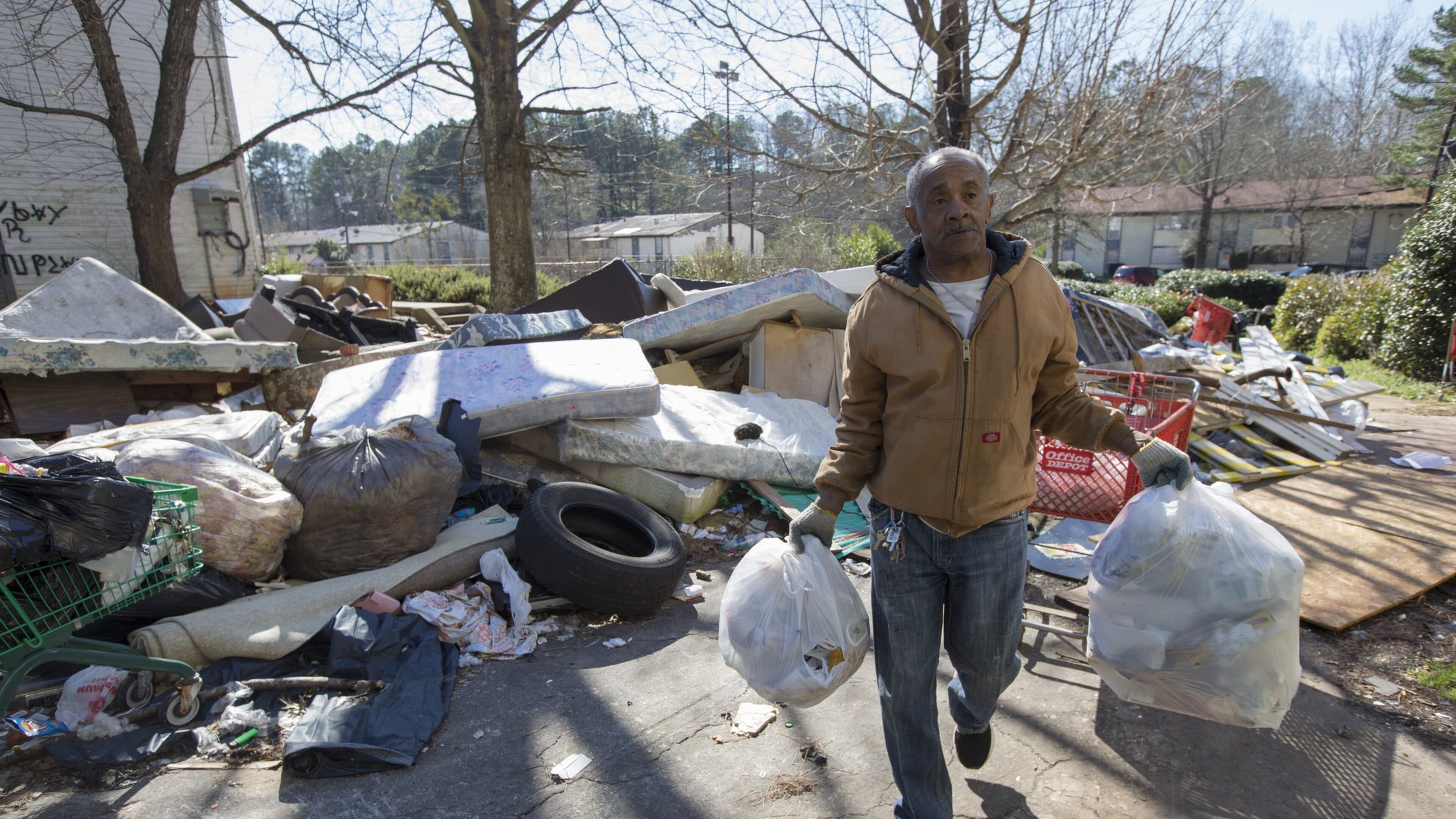 Despite the piles of trash, furniture and tires around him, James Starr, who has lived at Brennon Hill for four years, carries his trash to a trash bin Feb 2. Ben Gray / bgray@ajc.com