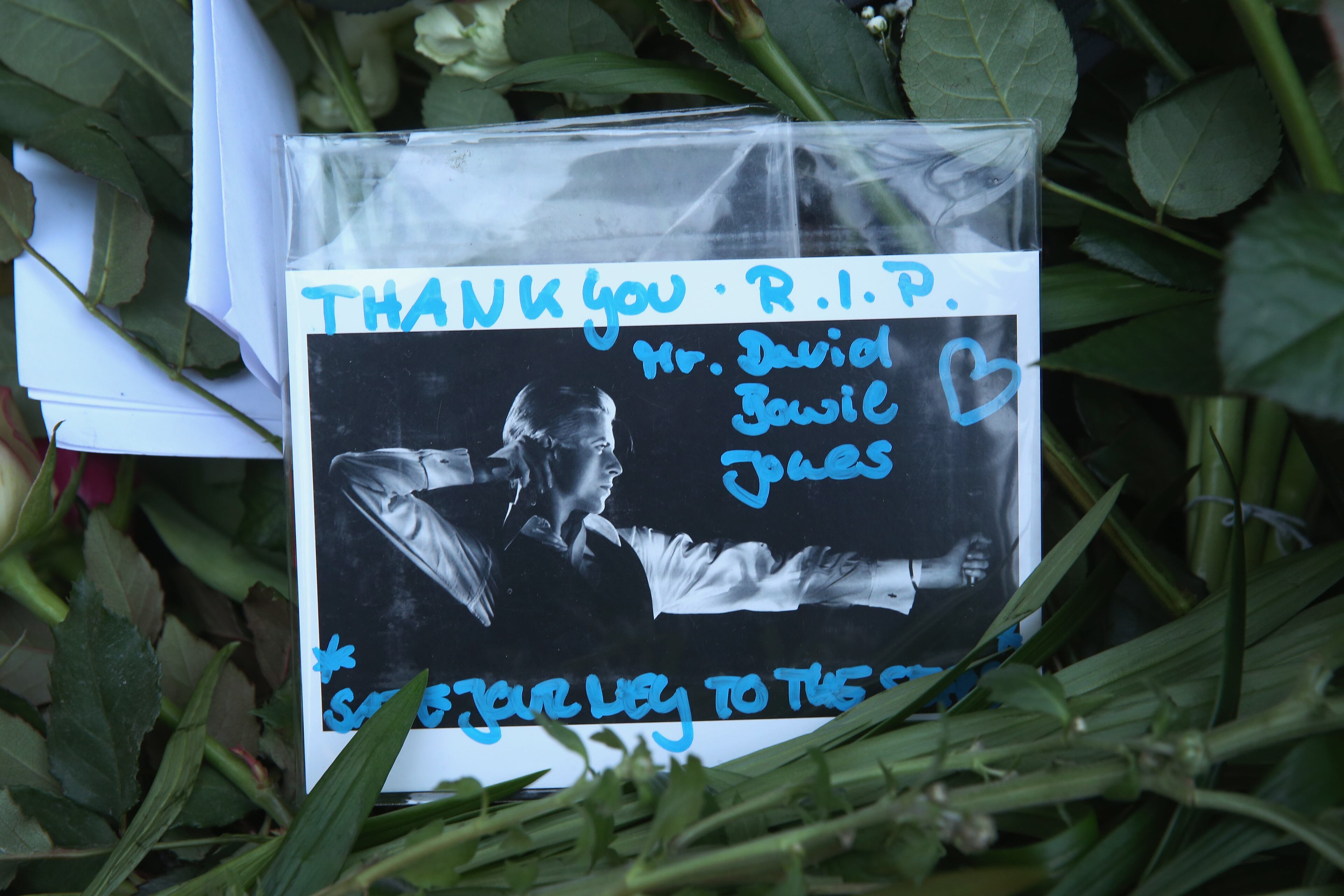 BERLIN, GERMANY - JANUARY 11: A photograph of British musician David Bowie lies among flowers and candles left by fans at the doorstep at the building where he once lived following the announcement of his death on January 11, 2016 in Berlin, Germany. Bowie lived and composed in West Berlin in the late 1970s. He died at the age of 69 following an 18-month struggle against cancer. (Photo by Sean Gallup/Getty Images)